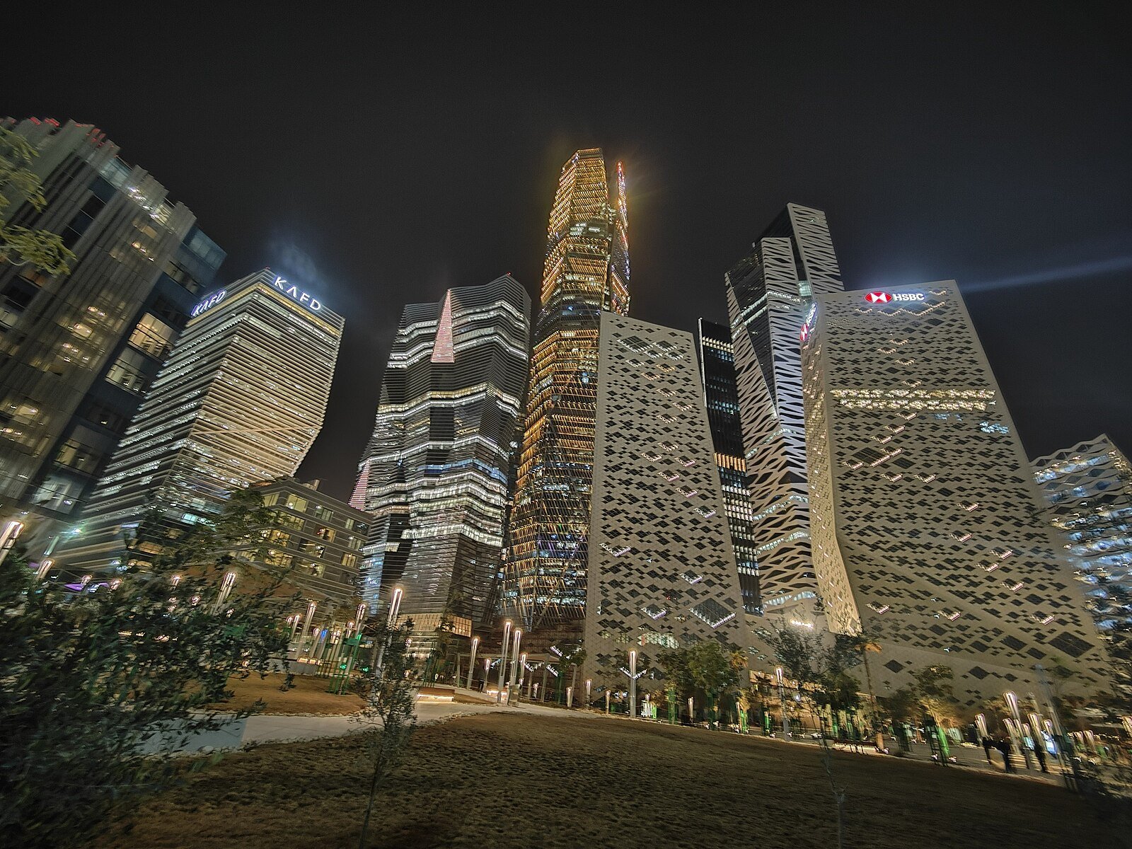 The illuminated towers of the King Abdullah Financial District in Riyadh, seen from the gardens at night.