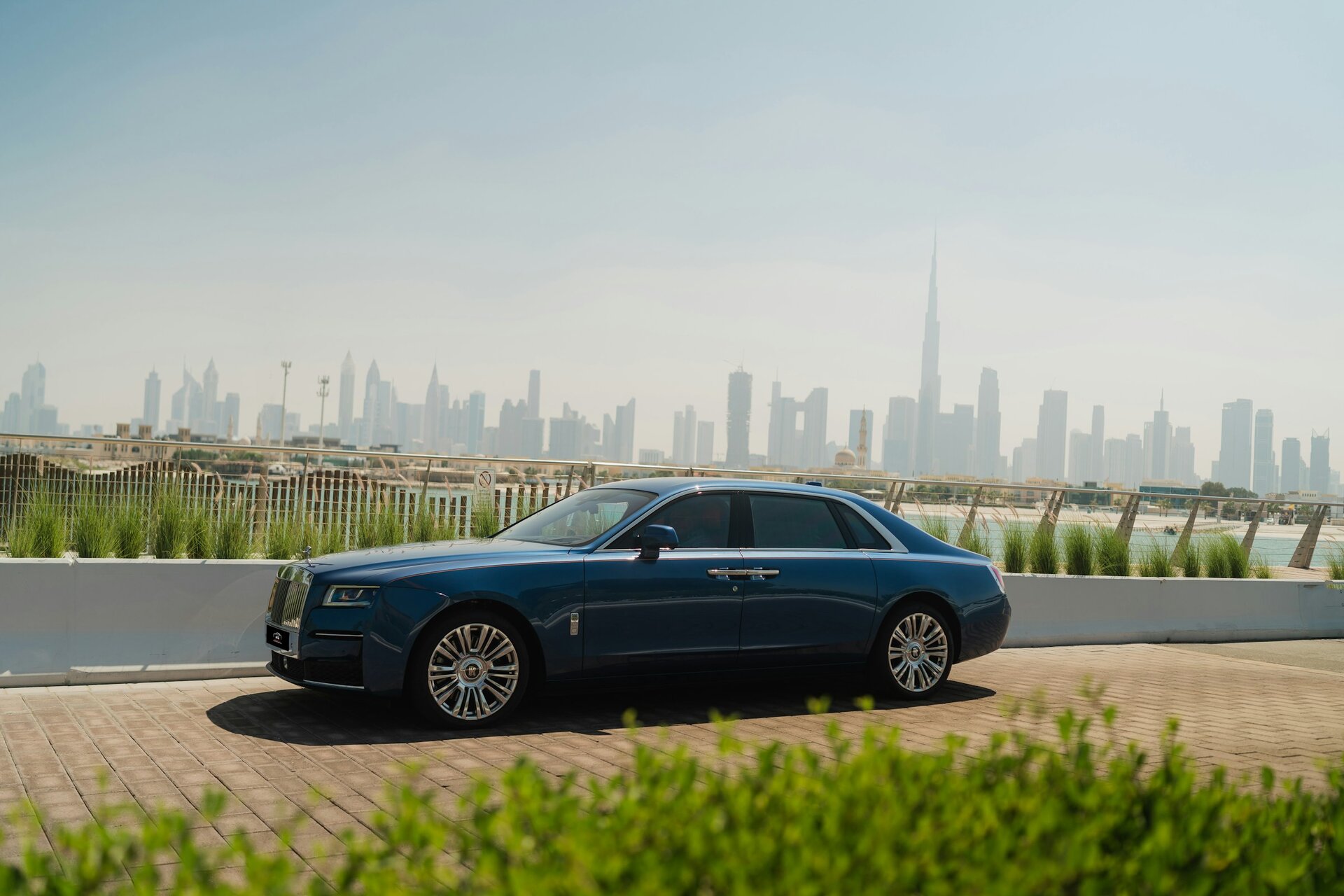 A Rolls-Royce Ghost by the water, with the Dubai skyline and Burj Khalifa behind