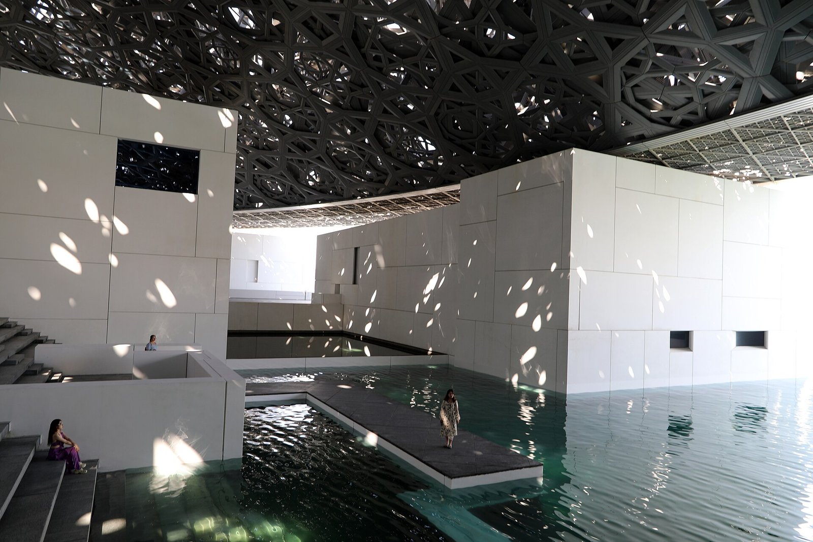 Dappled light falls through the latticed dome of the Louvre Abu Dhabi onto its white galleries and reflecting pools on Saadiyat Island.