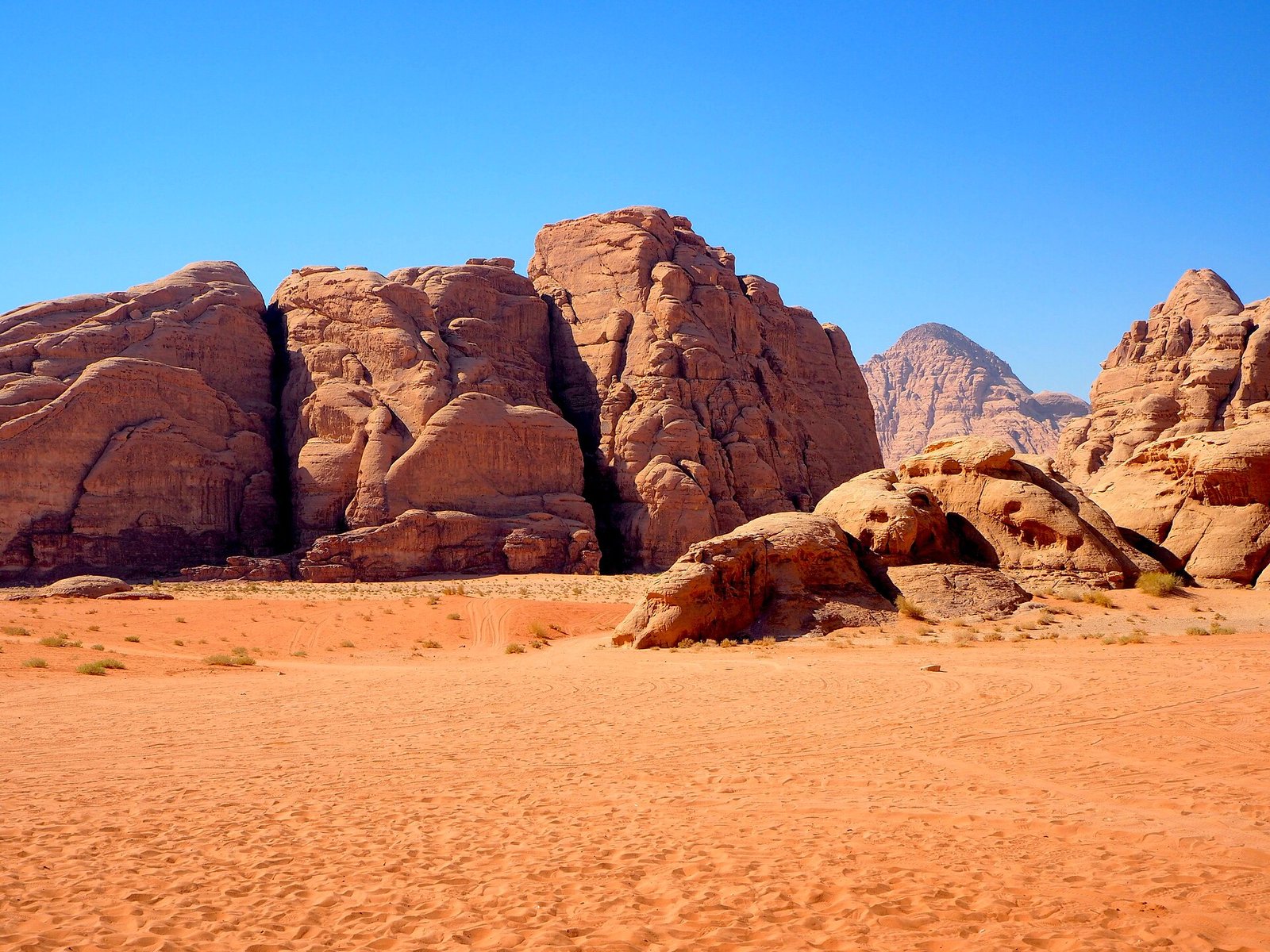 Red sandstone outcrops rising from the orange sands of Wadi Rum, Jordan, under a deep blue sky