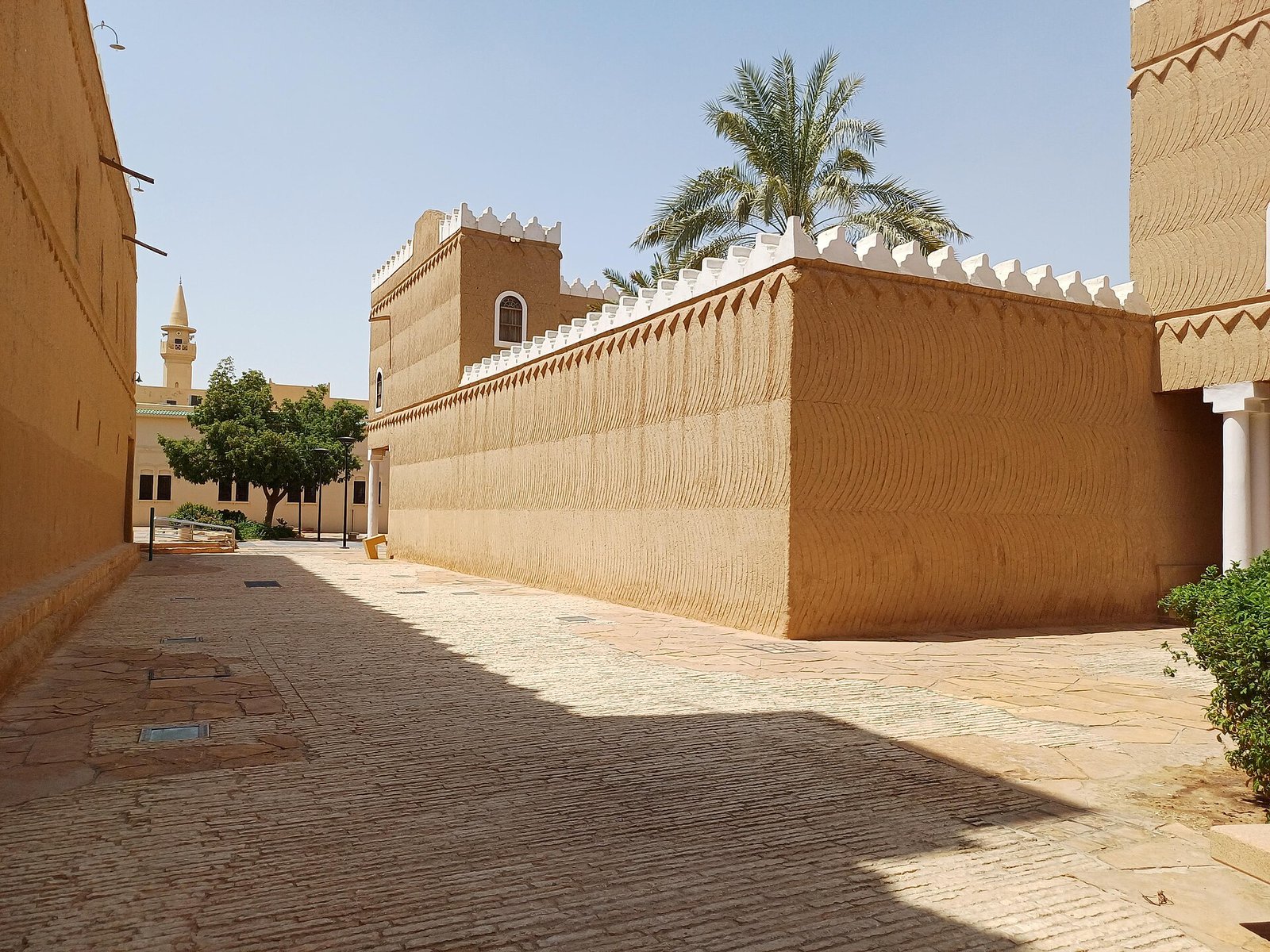 Crenellated mud-brick walls line a sunlit lane at Murabba Palace, King Abdulaziz's palace in Riyadh.