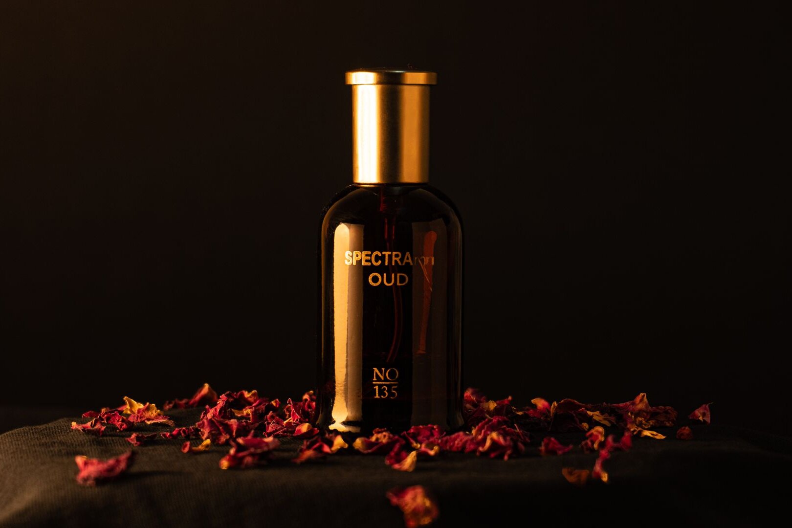 A bottle of oud perfume among dried rose petals