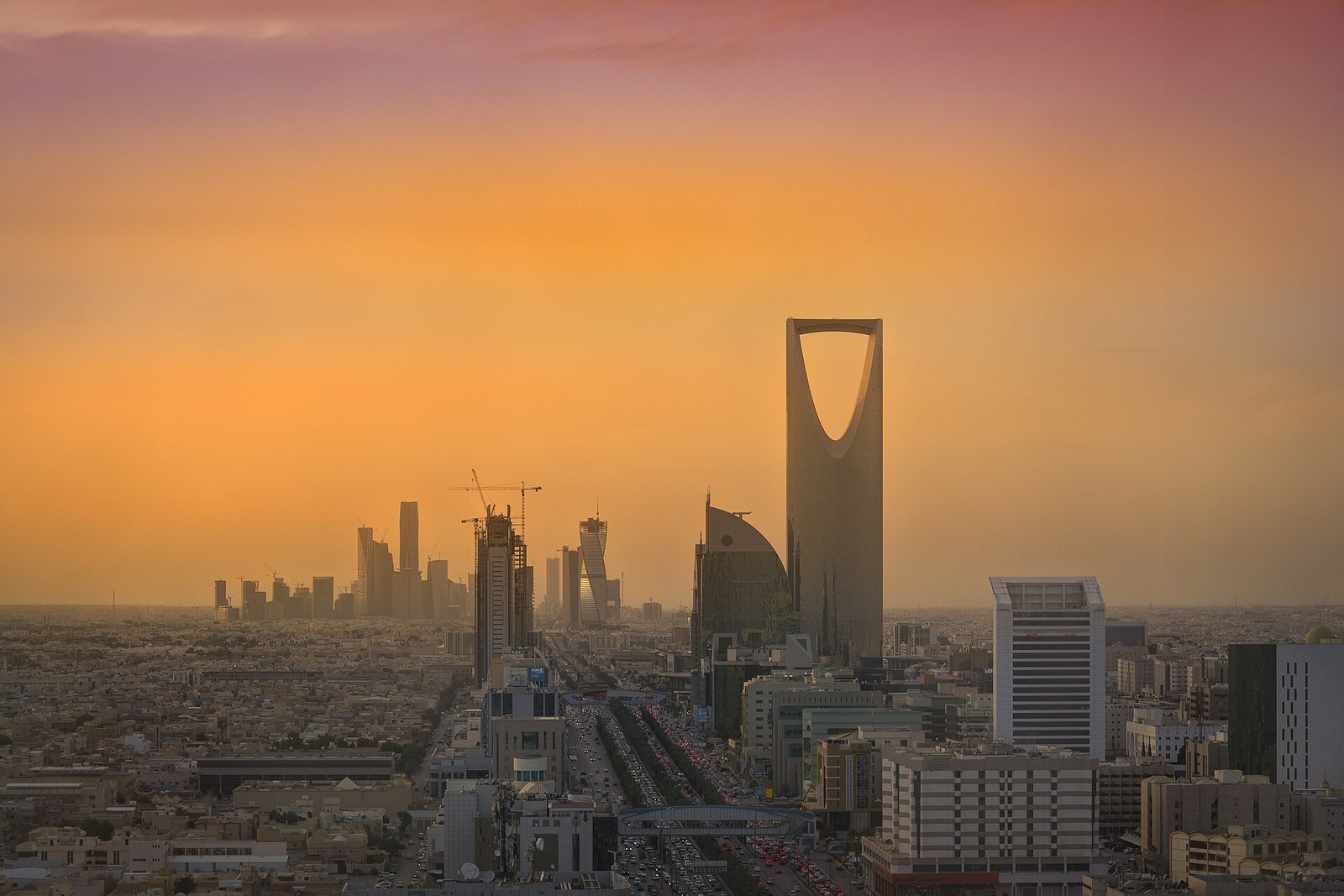 The Kingdom Centre and the Riyadh skyline glowing under an amber sunset sky.