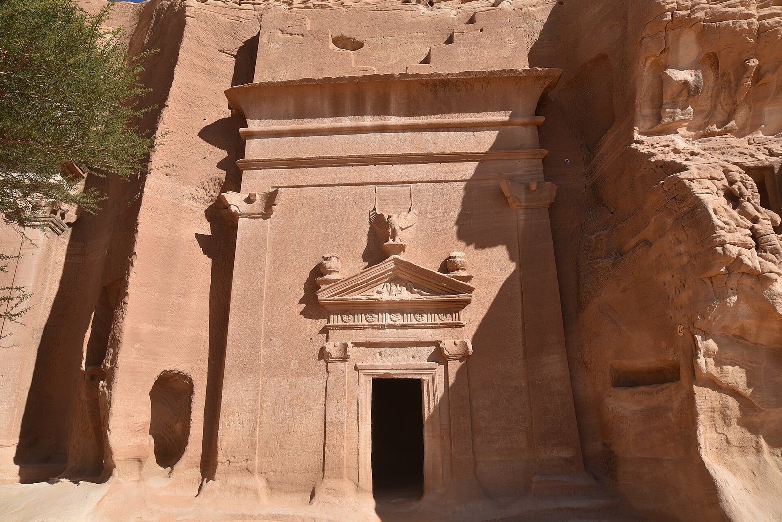 A Nabataean tomb facade with carved pediment and eagle cut into a sandstone outcrop at Hegra, Saudi Arabia.