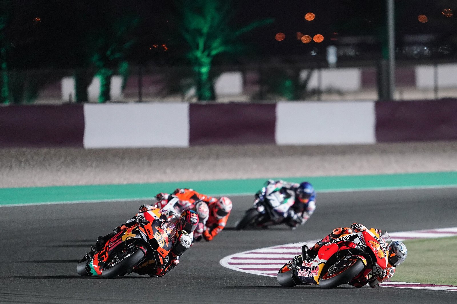 MotoGP riders lean into a floodlit corner at night at the Lusail International Circuit in Qatar.