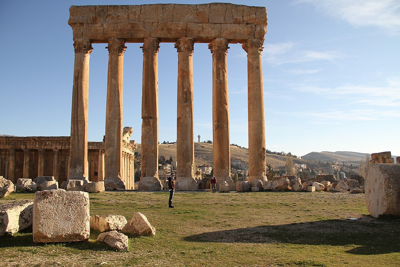 The six surviving Roman columns of the Temple of Jupiter at Baalbek rising above the ruins under a blue sky.