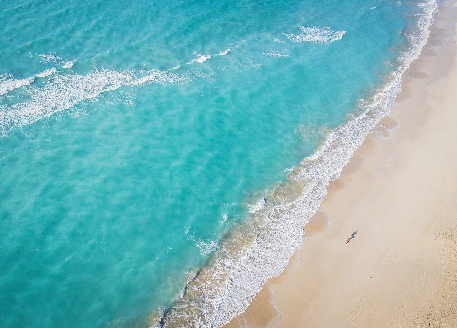Turquoise surf breaking along the white sand of Saadiyat Island's beach, seen from above.