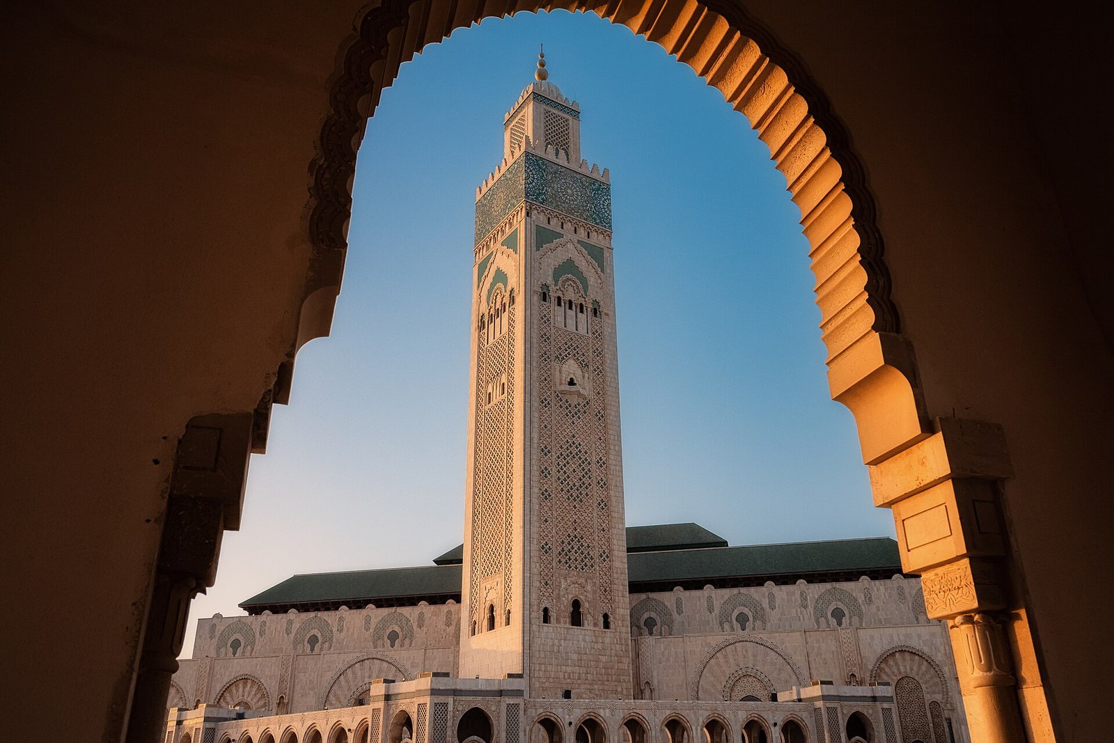 The minaret of the Hassan II Mosque in Casablanca, framed by a carved archway in the evening light.
