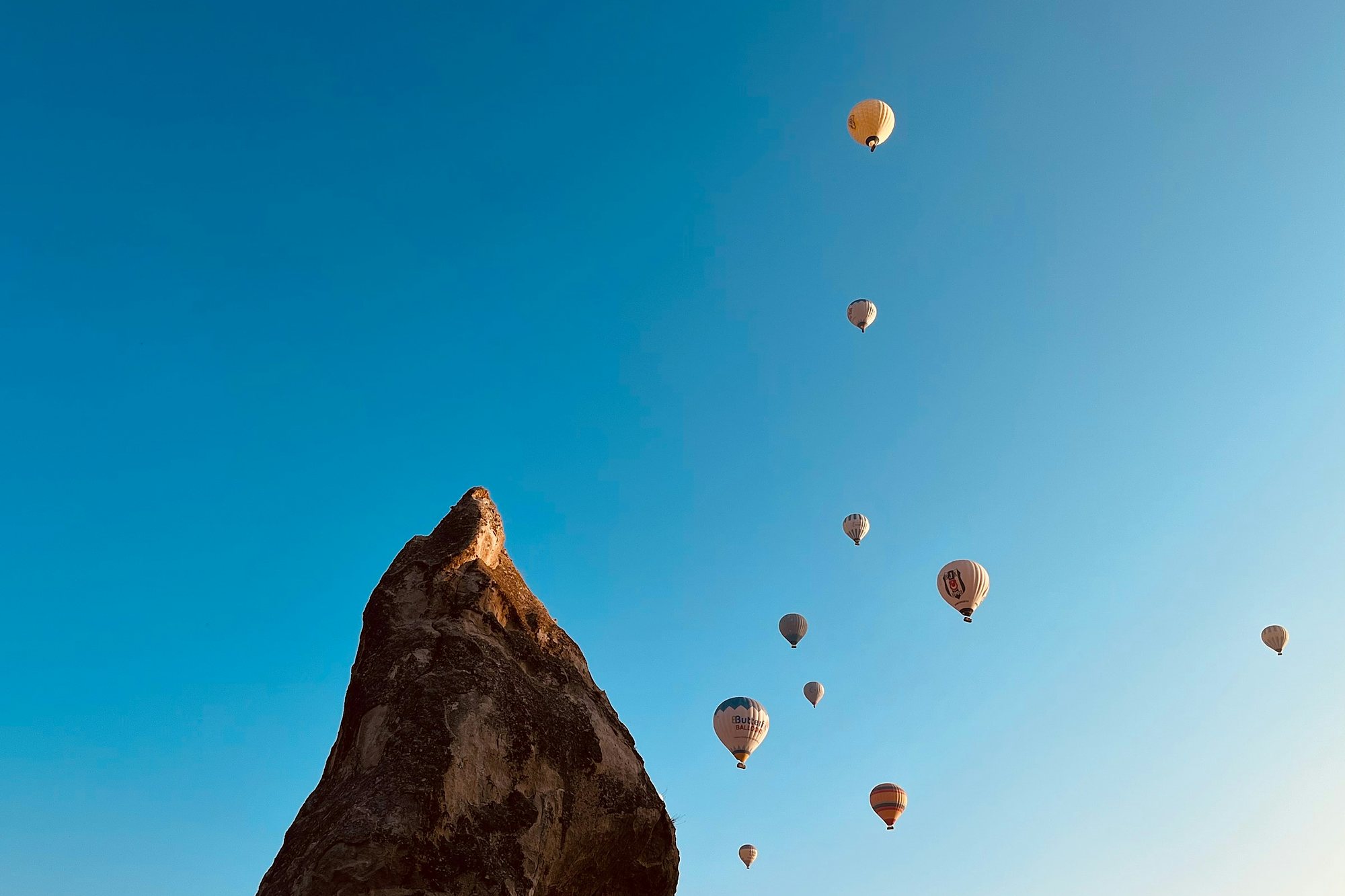 Hot-air balloons rising past a fairy chimney in Cappadocia