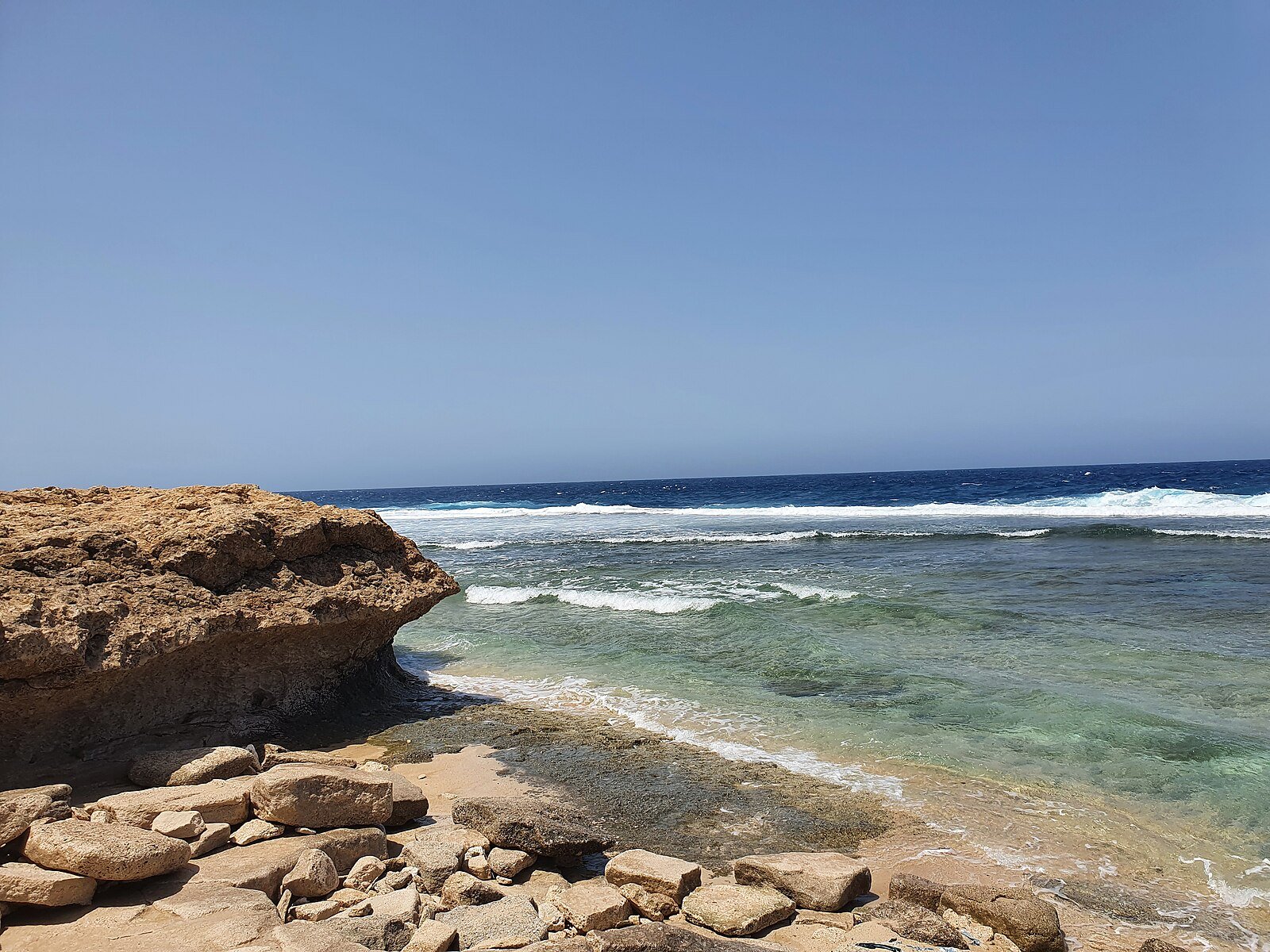 Clear turquoise water lapping a rocky limestone shore on the Red Sea coast at Umluj, Saudi Arabia.
