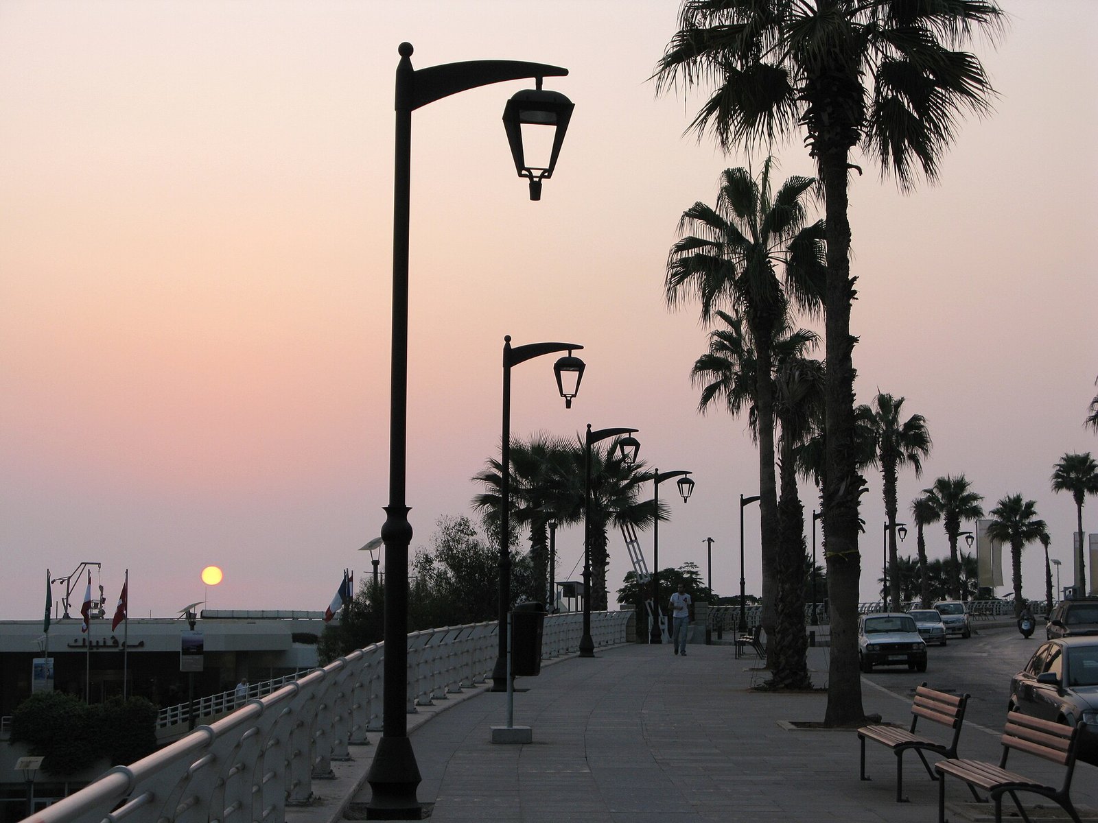 Palm trees and lamp posts line the Beirut Corniche as the sun sets over the Mediterranean.
