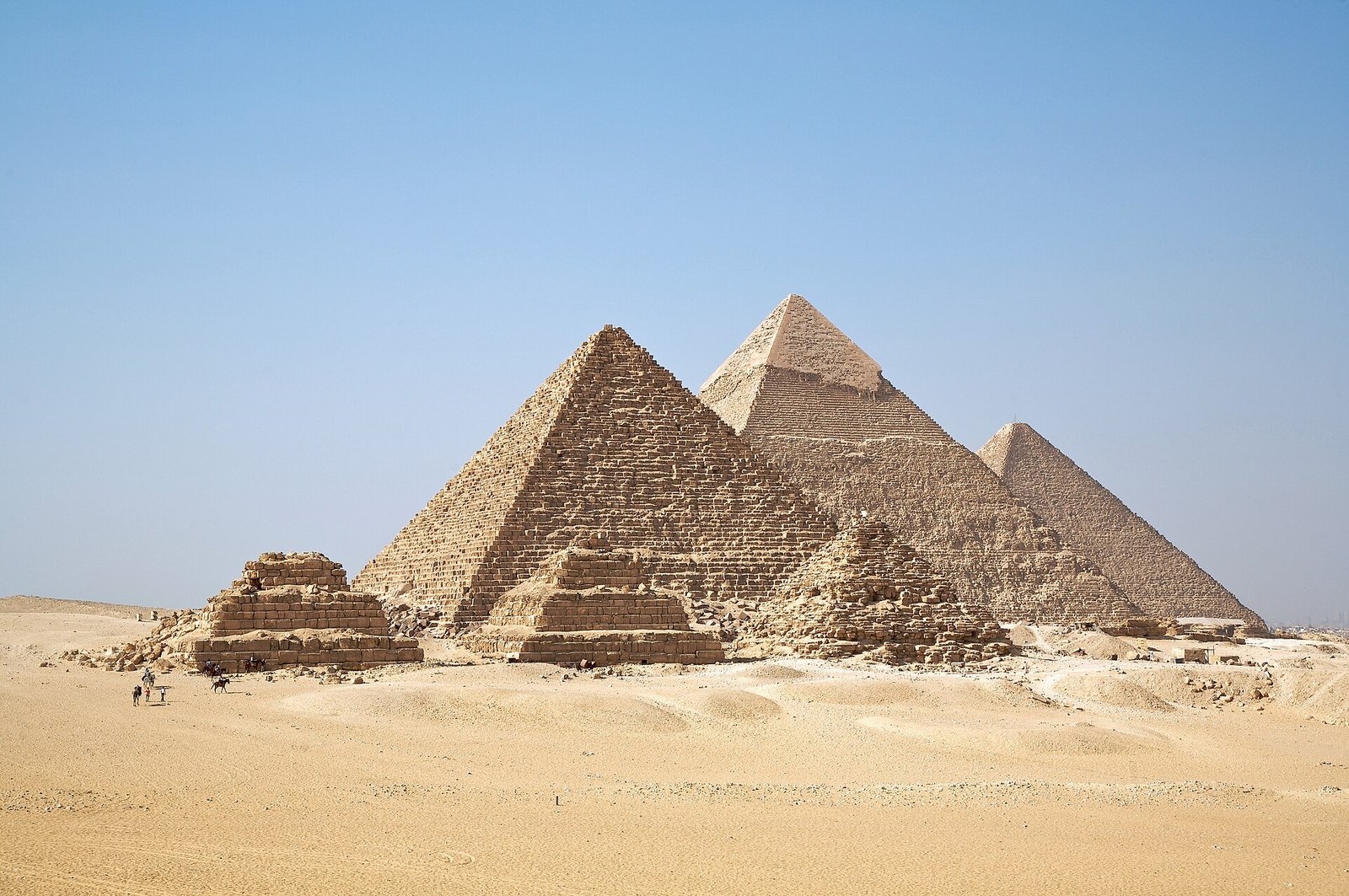 The three great pyramids of Giza and the smaller Queens' pyramids rise from the desert under a clear blue sky.