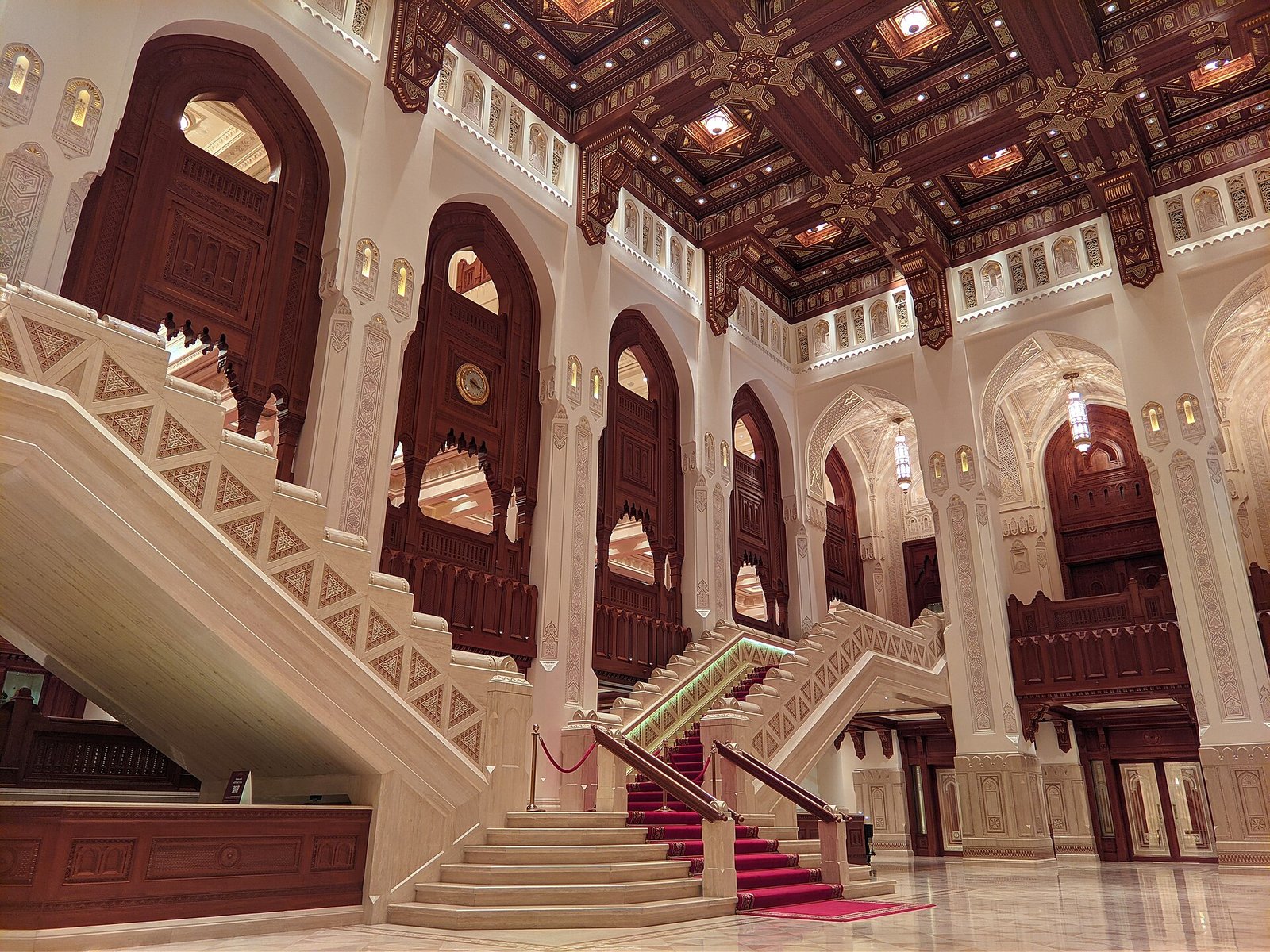 Carved arches, a coffered wooden ceiling and a sweeping marble staircase in the foyer of the Royal Opera House Muscat.