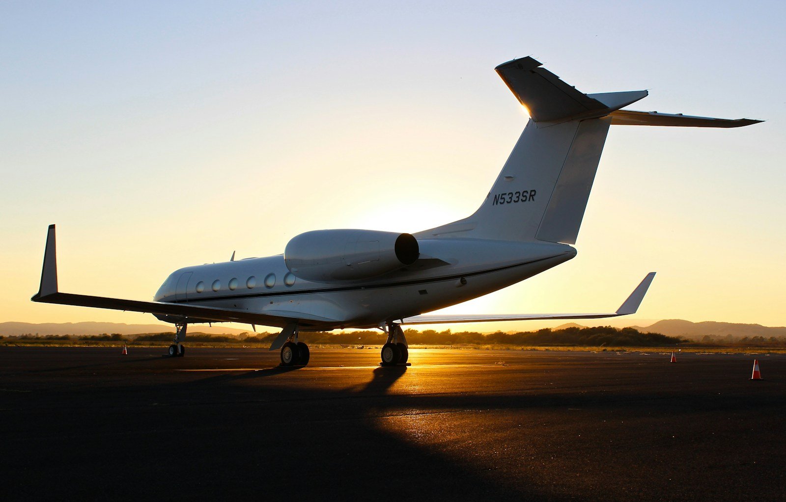 A Gulfstream business jet silhouetted on the tarmac against a golden sunset.