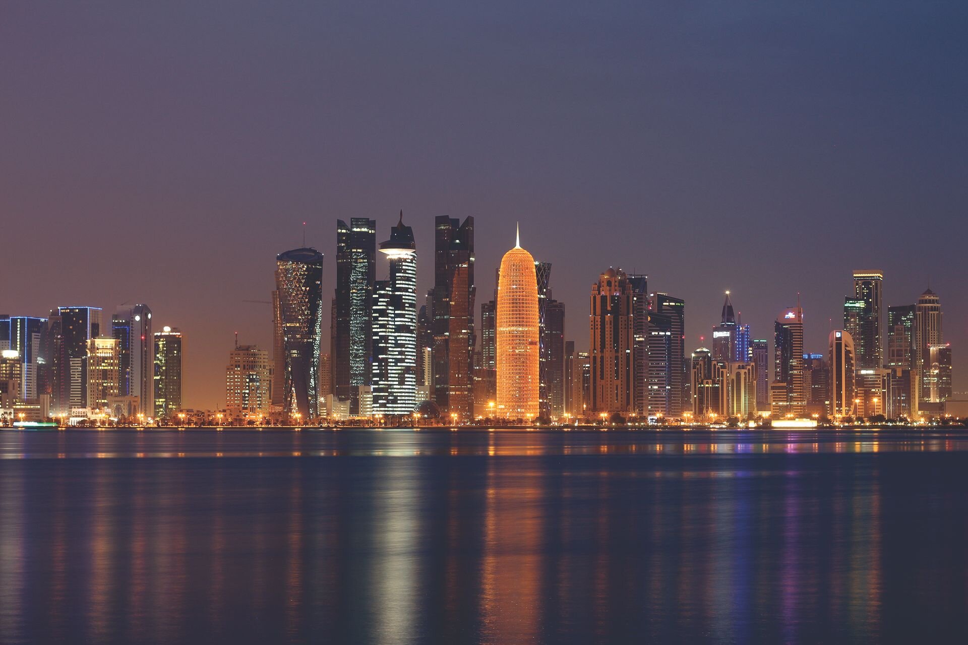 The West Bay skyline of Doha lit up at night, reflected in the bay