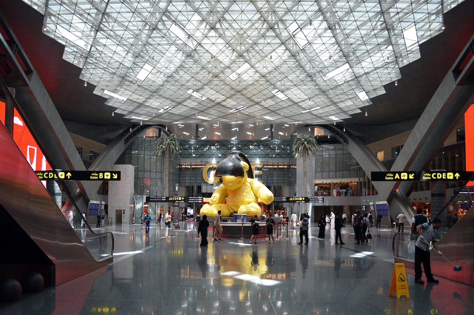 The soaring glass-roofed duty-free hall of Hamad International Airport in Doha, with its giant golden Lamp Bear sculpture.