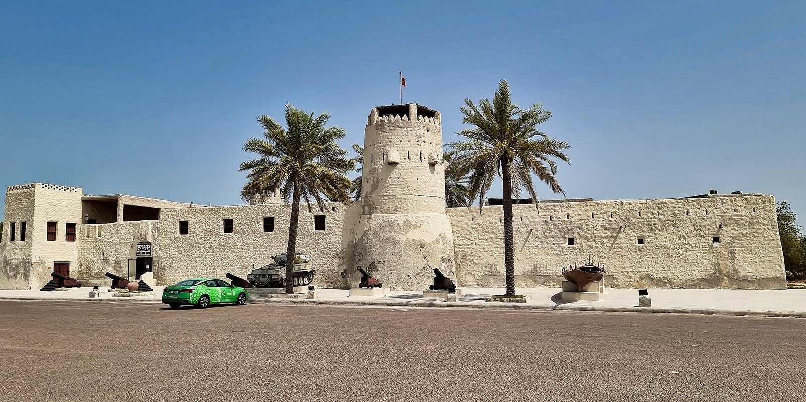 The white walls and round watchtower of Umm Al Quwain Fort, the historic seat of the Al Mualla rulers, framed by palms.