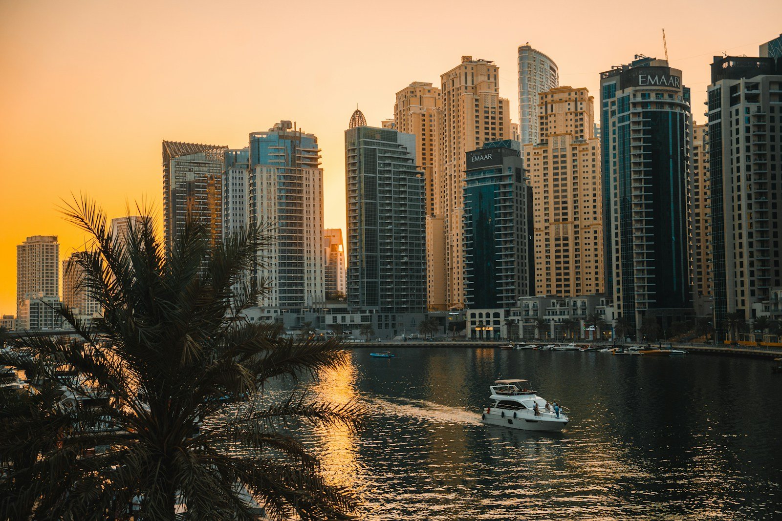 A motor yacht glides along Dubai Marina at golden hour beneath its waterfront residential towers.