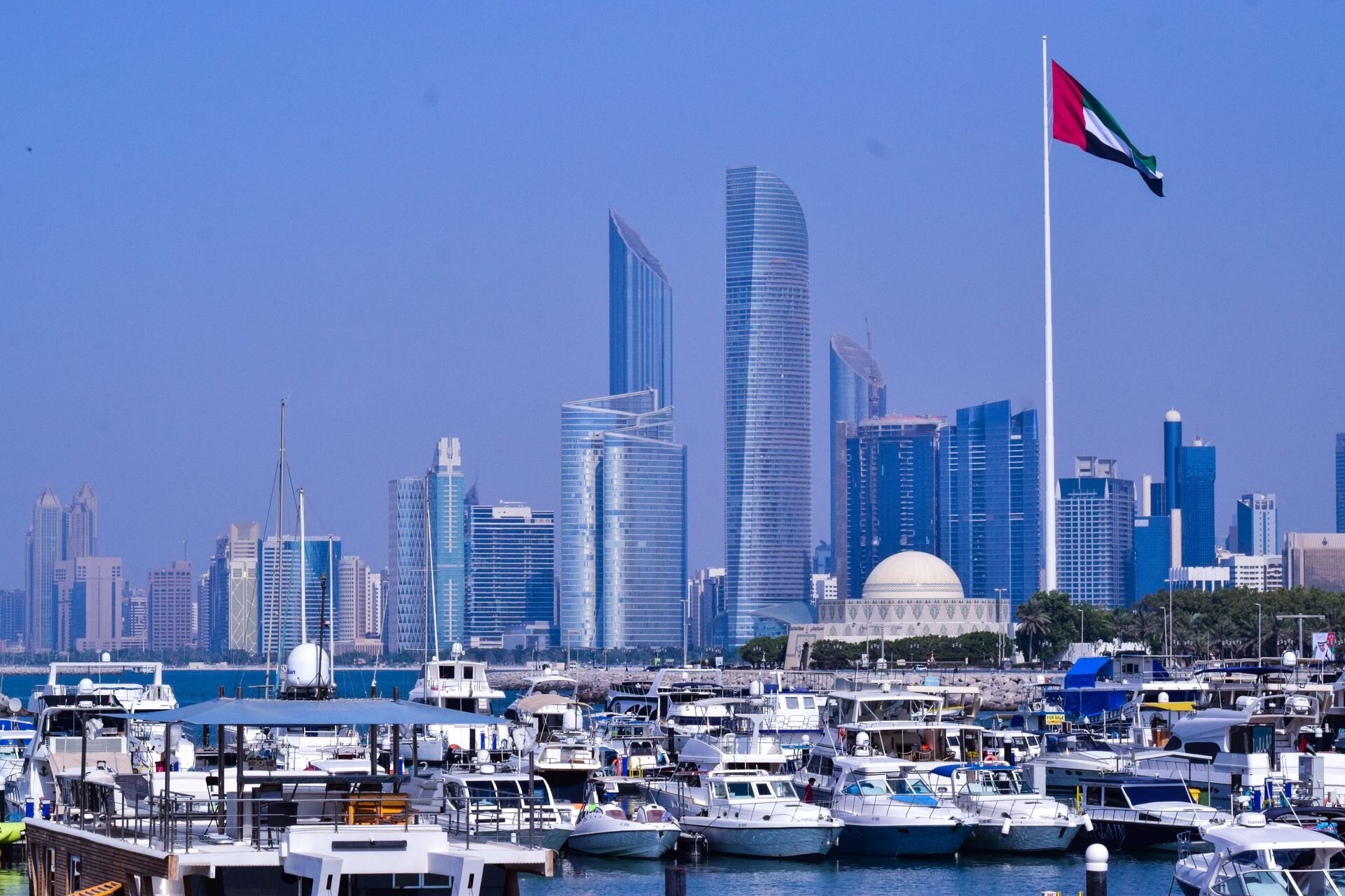The UAE flag above a marina on the Abu Dhabi Corniche, with the city's towers behind