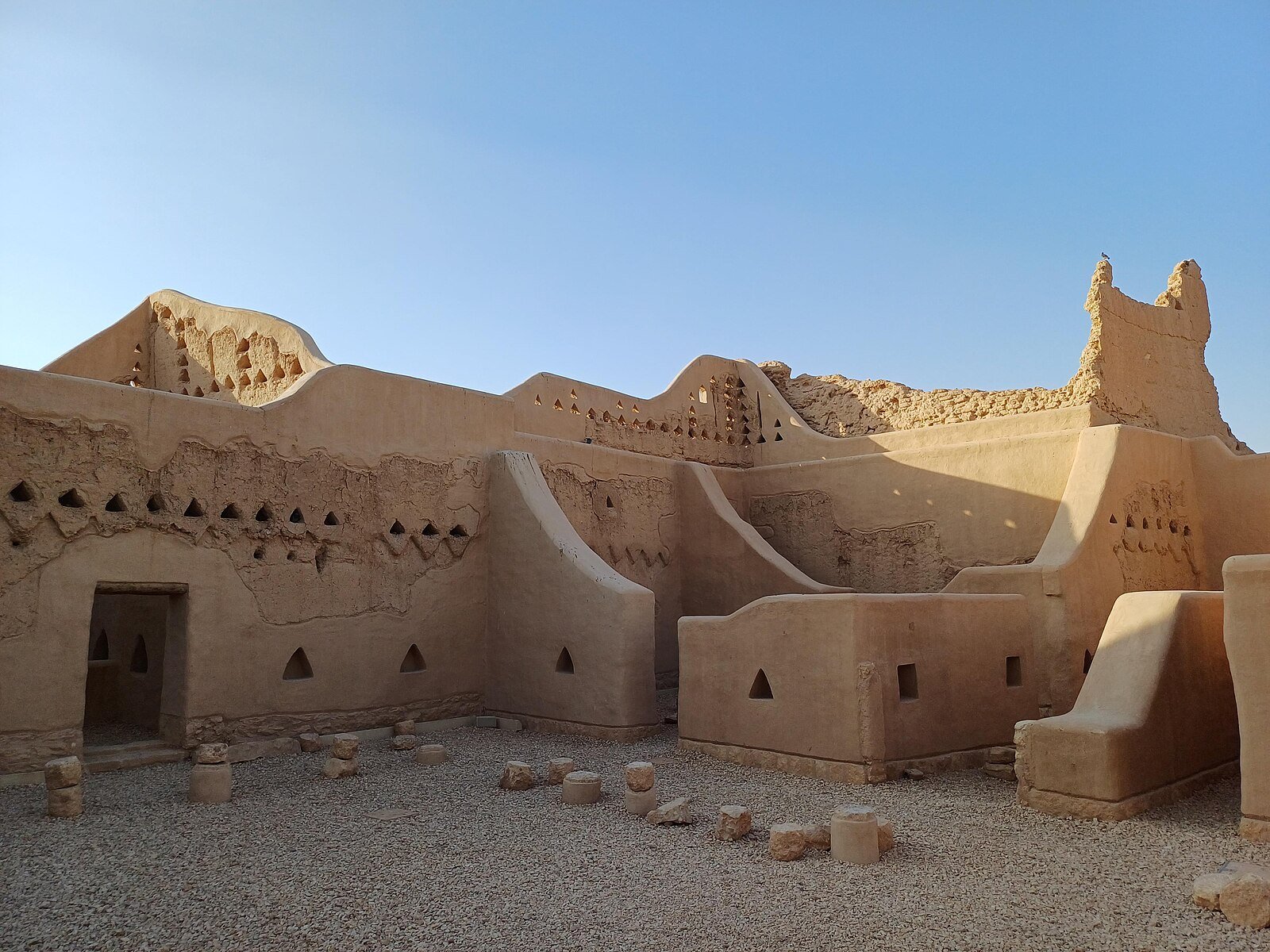 Sculpted mud-brick walls and towers of the At-Turaif district in Diriyah, the UNESCO-listed birthplace of the Saudi state, under a clear blue sky.