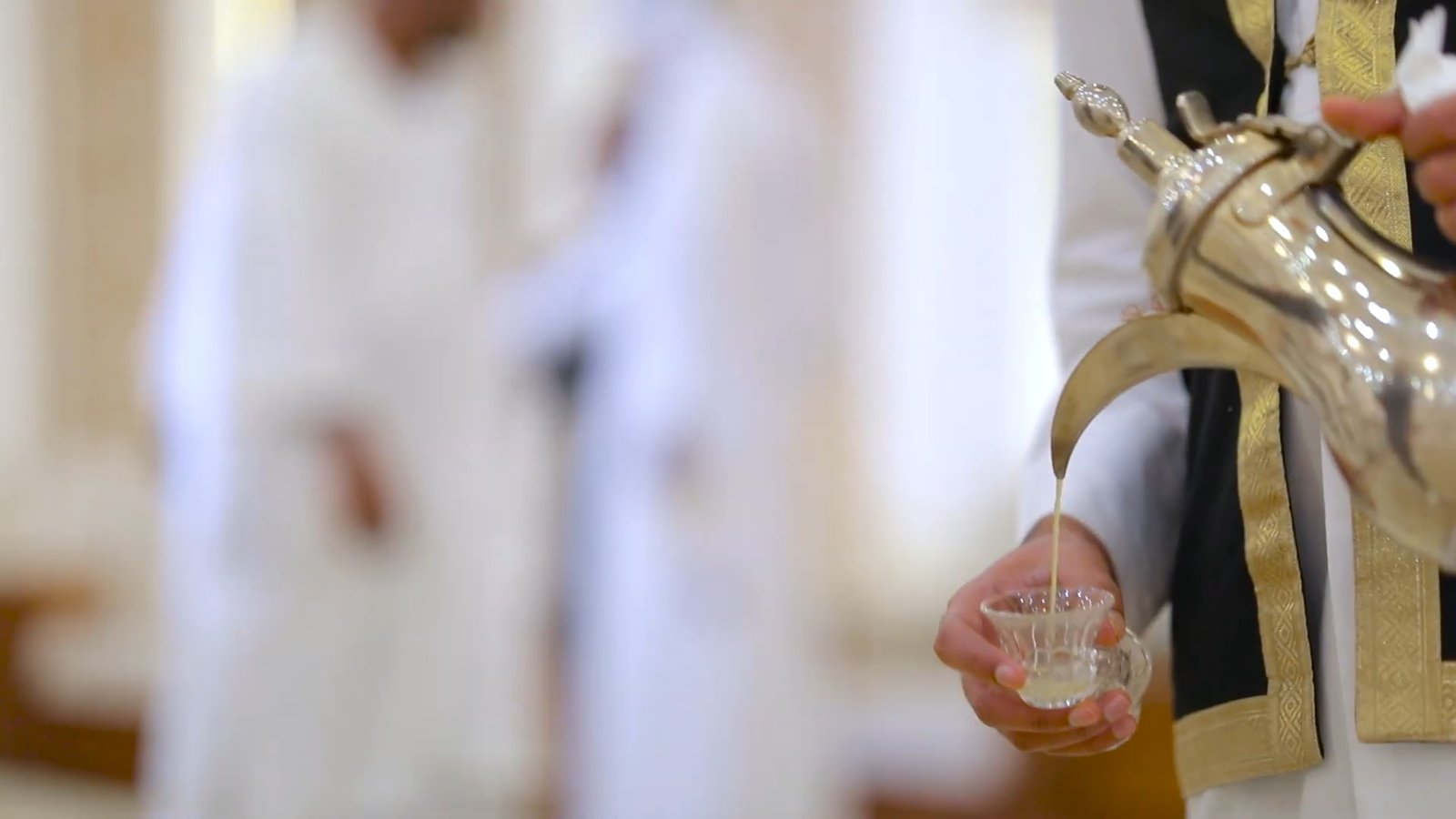 A host pours Arabic coffee, gahwa, from a silver dallah into a small cup for a guest.