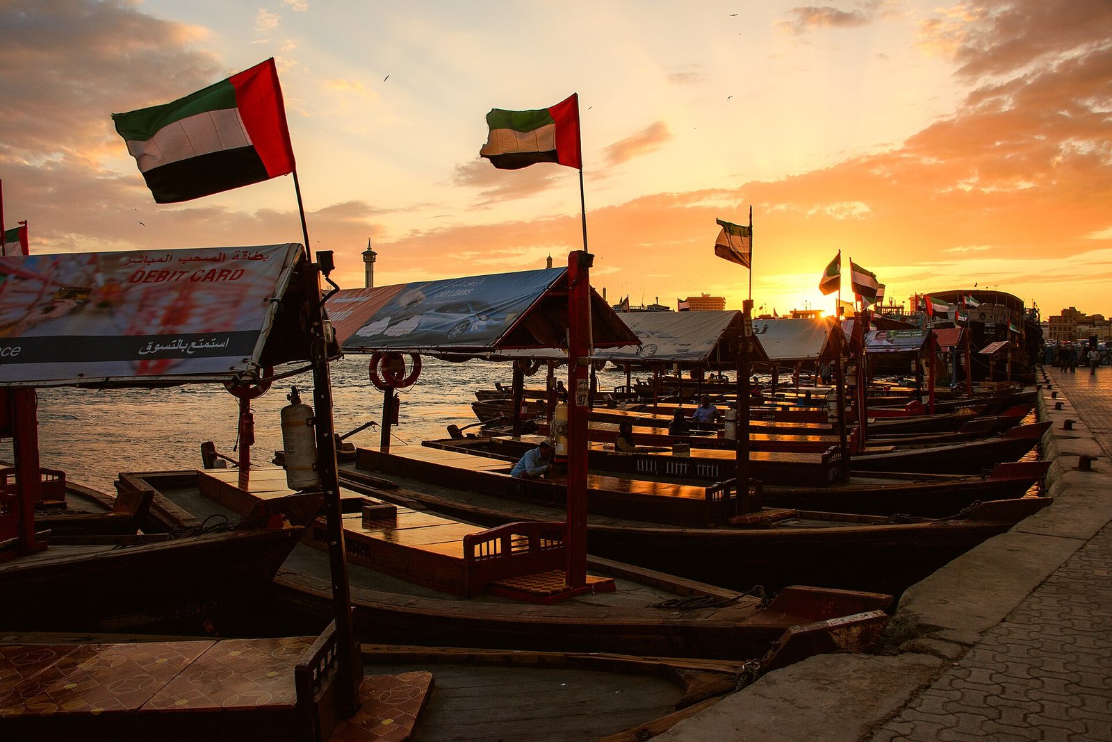Traditional abra water taxis flying UAE flags along Dubai Creek at sunset.