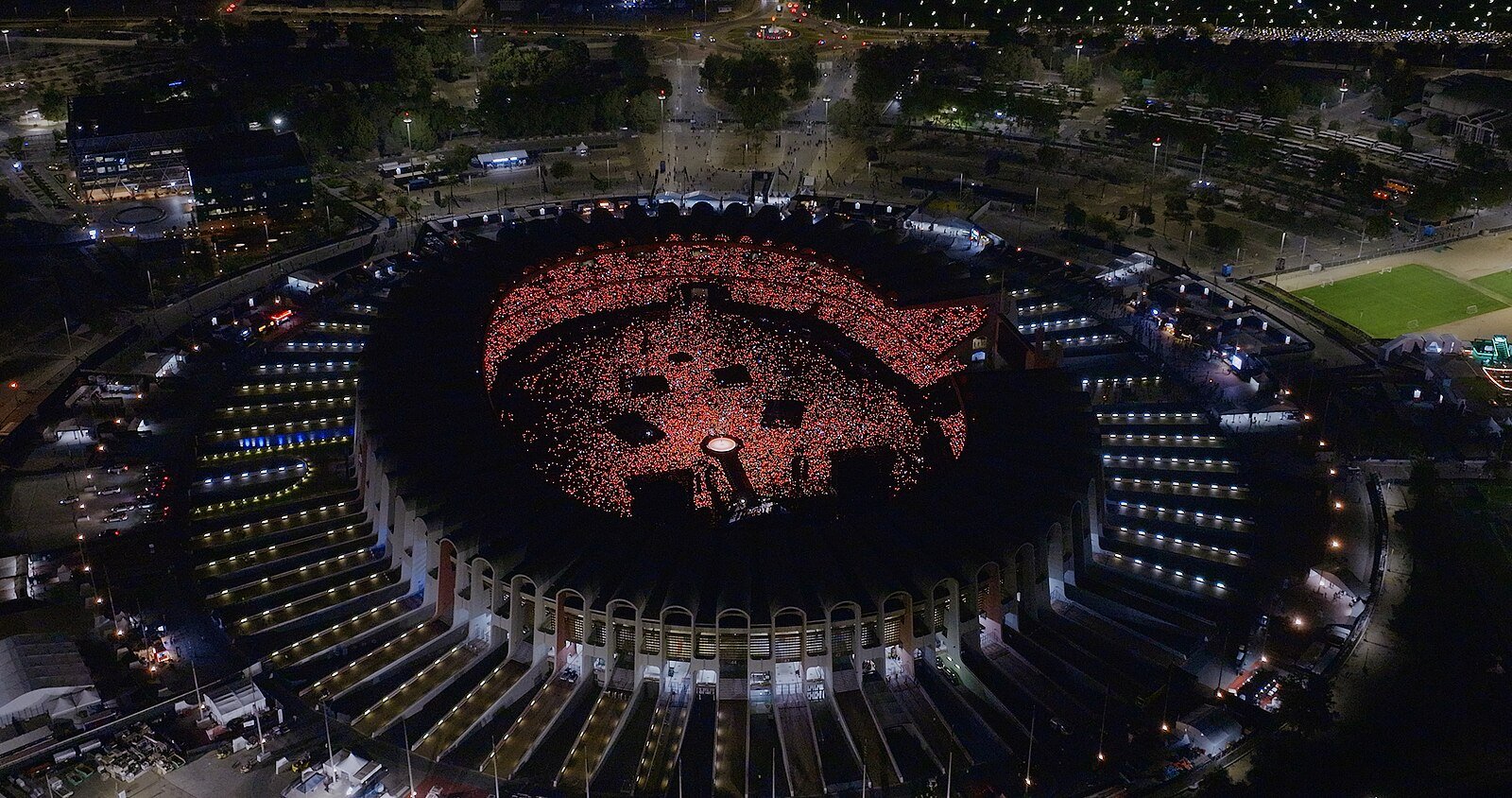 Zayed Sports City Stadium in Abu Dhabi seen from above at night, its bowl glowing red during a concert.
