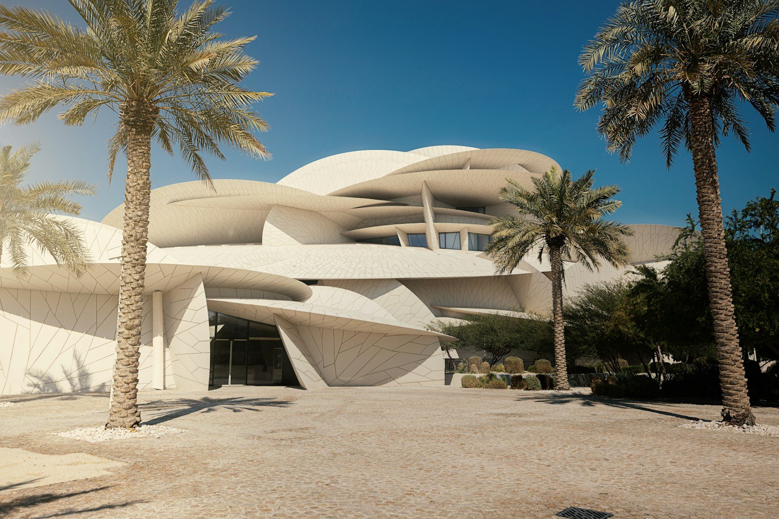 The interlocking desert-rose discs of Jean Nouvel's National Museum of Qatar framed by date palms under a deep blue sky, Doha.