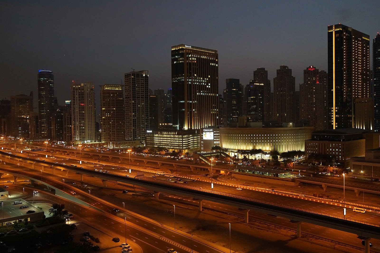 Sheikh Zayed Road glows with evening traffic below the lit towers of Jumeirah Lake Towers and Dubai Marina.
