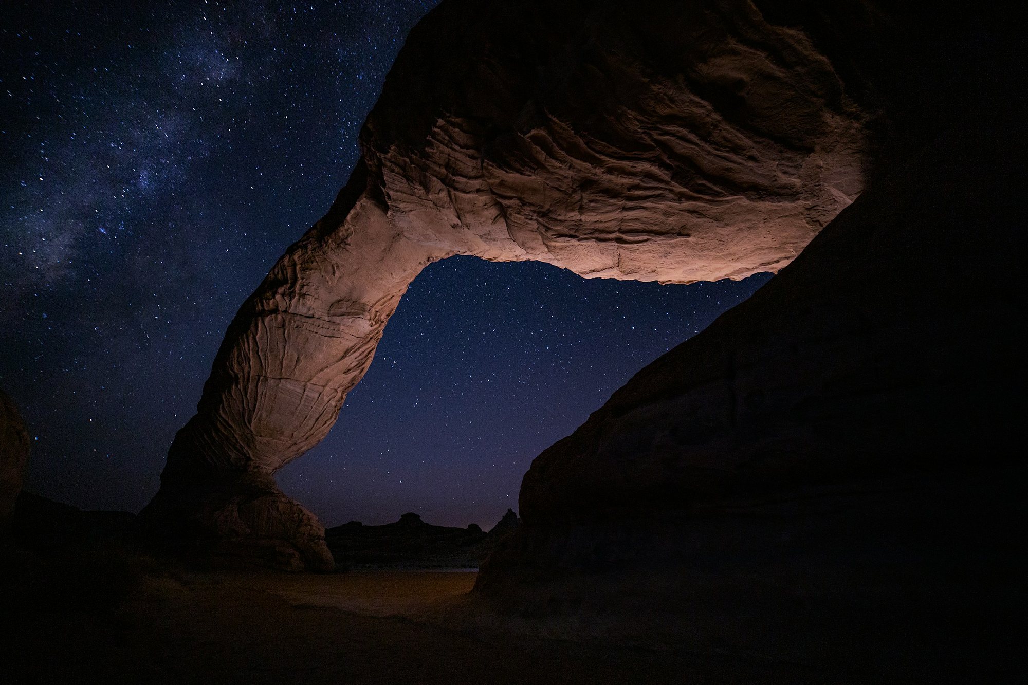 A sandstone arch under the Milky Way in the Tabuk desert