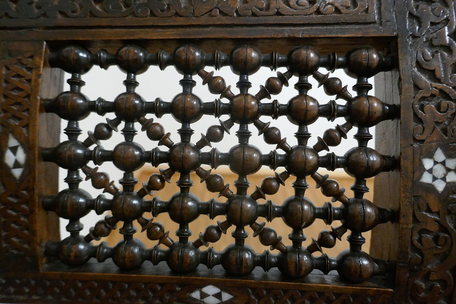 A turned-wood mashrabiya lattice screen framed by carved, inlaid woodwork.