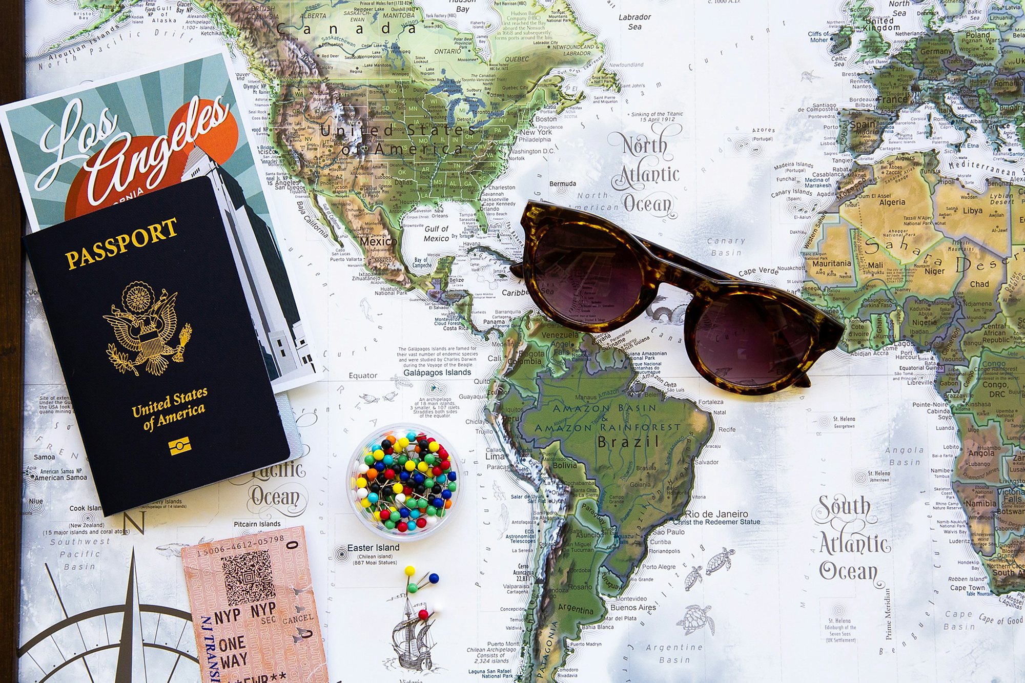 A passport, sunglasses and map pins on a world map