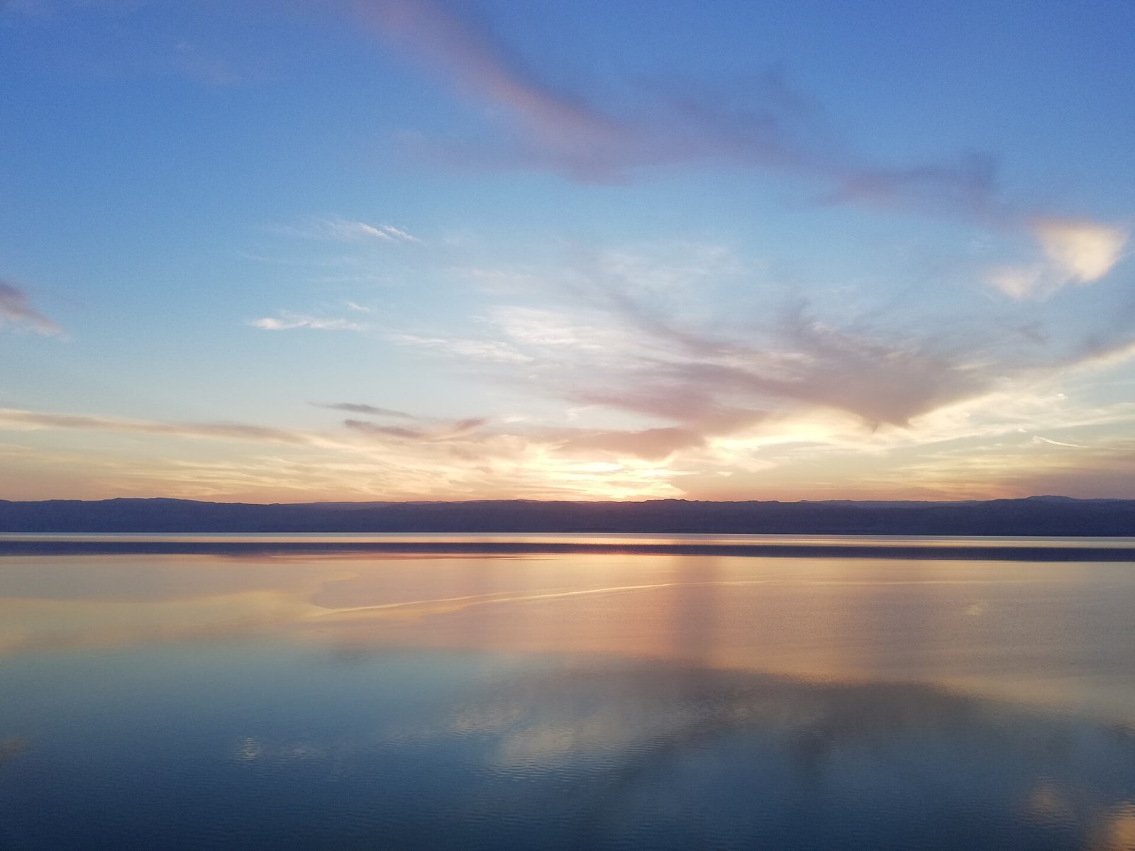 Pastel clouds at sunset mirrored in the glassy surface of the Dead Sea.