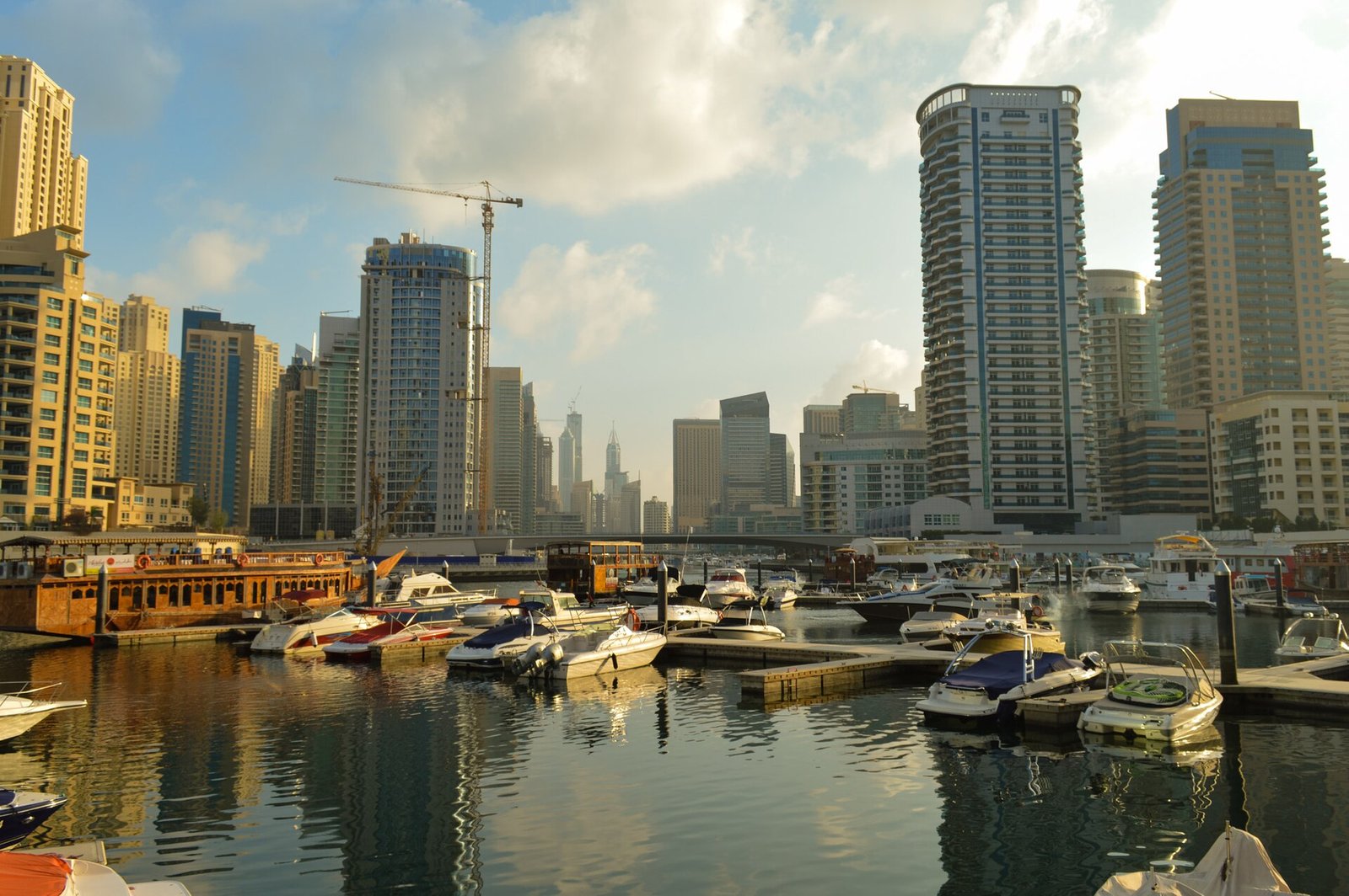 Yachts moored in still water at the southern end of Dubai Marina, beneath the marina's towers in late-afternoon light.