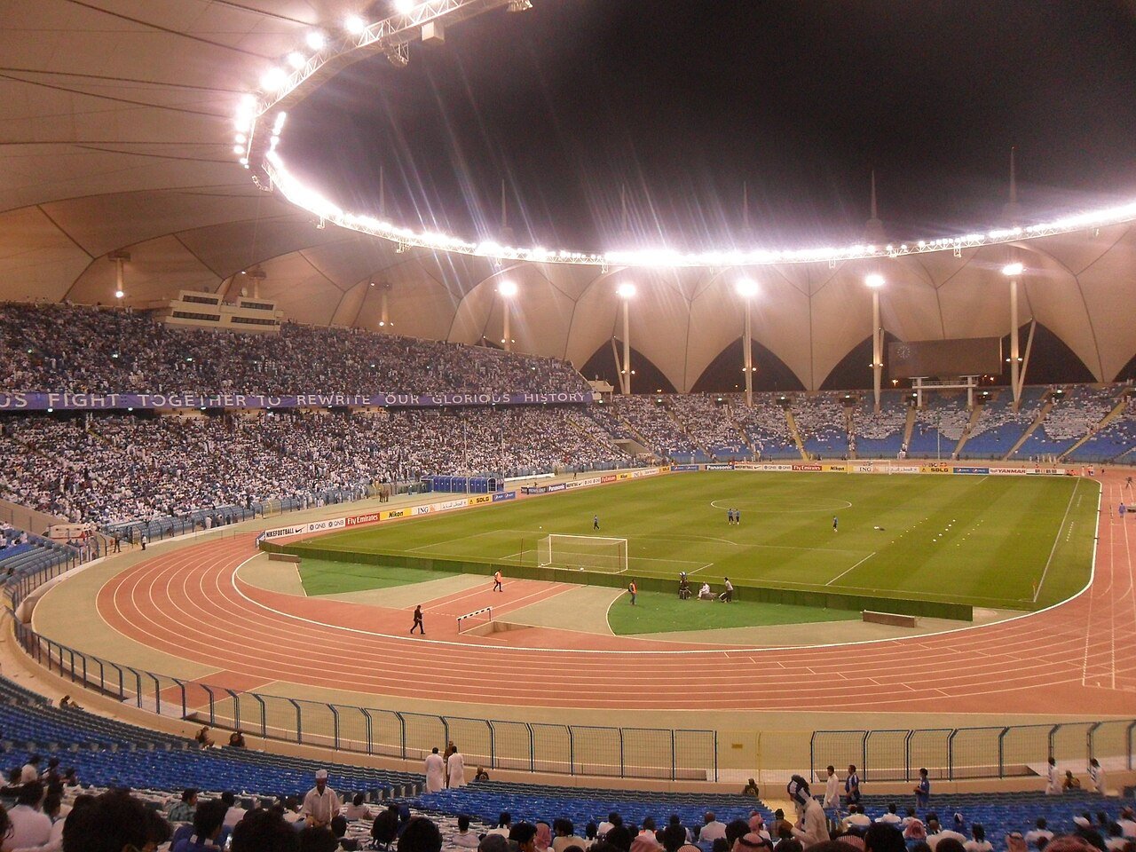 The floodlit bowl and tented canopy of King Fahd International Stadium in Riyadh during an evening match.