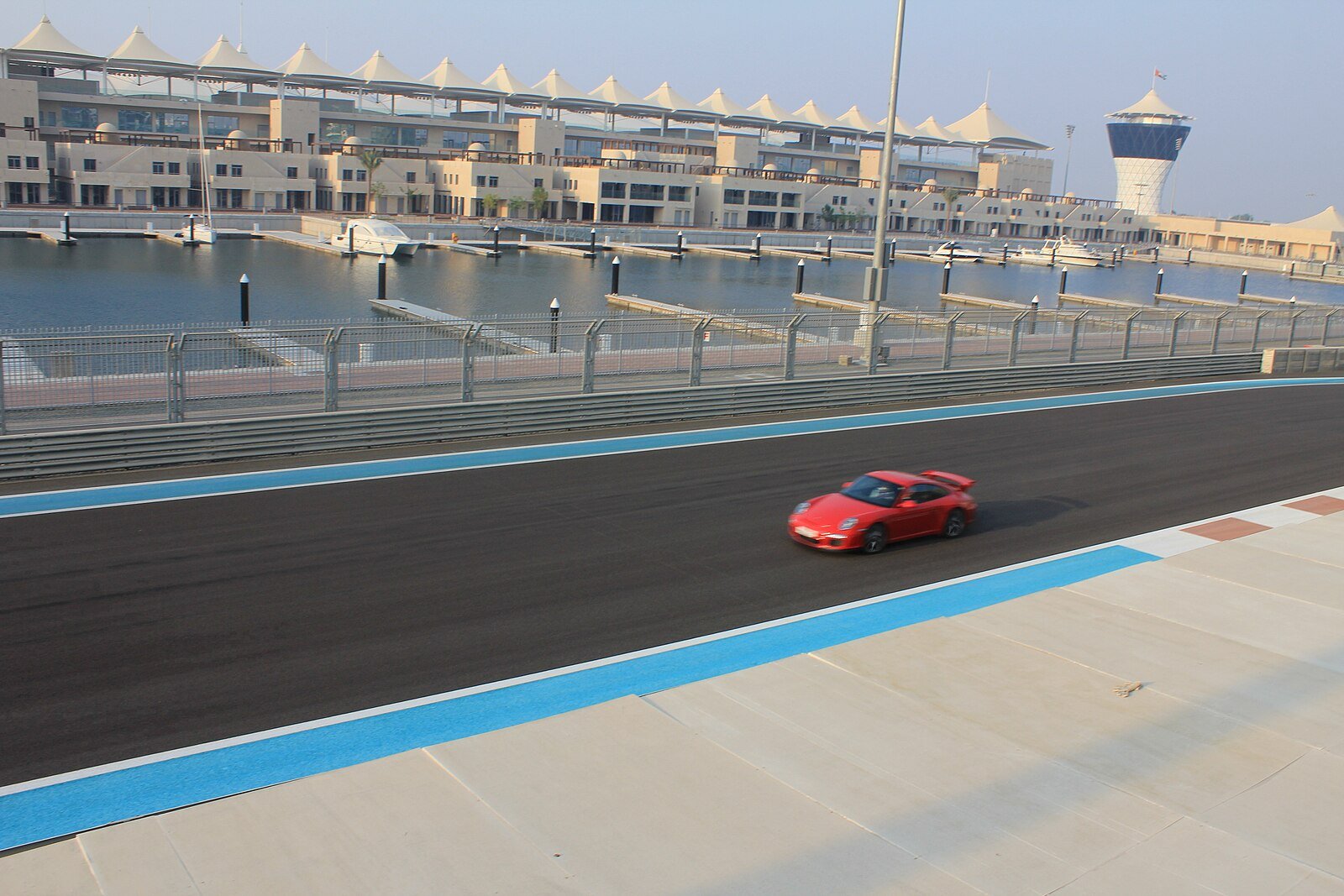 A red sports car on the Yas Marina Circuit, with yacht berths and the race-control tower of Yas Marina beyond