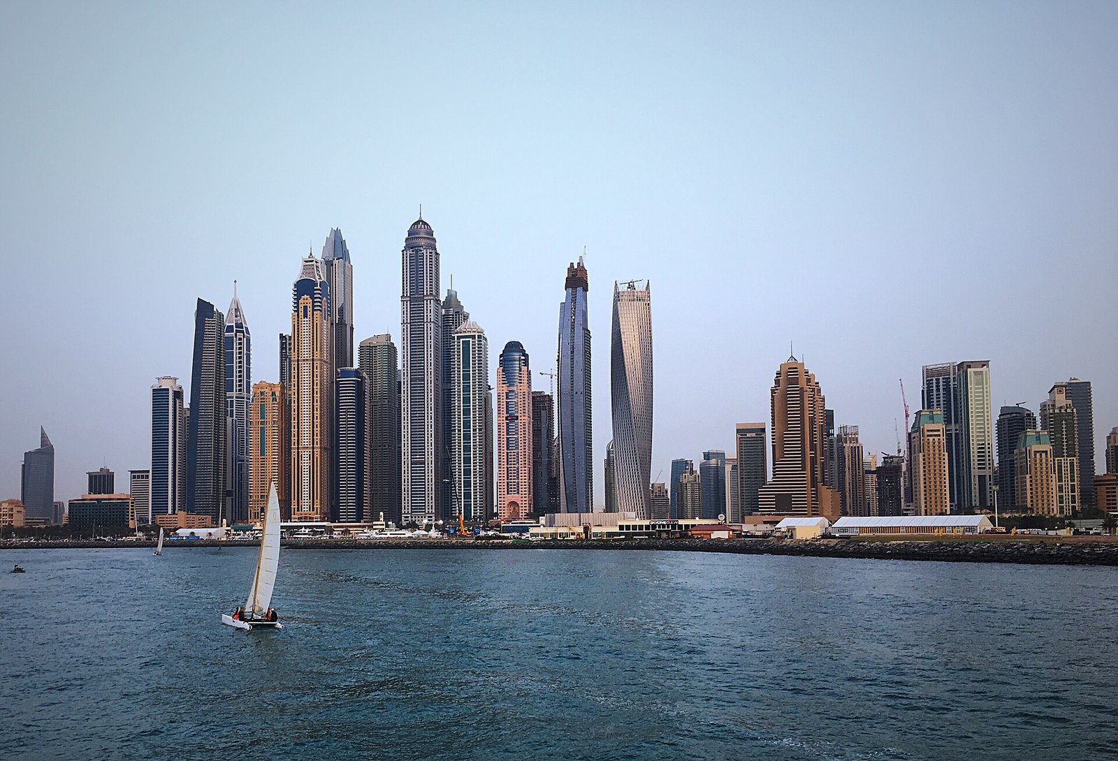 A sailboat on the water before the towers of Dubai Marina.