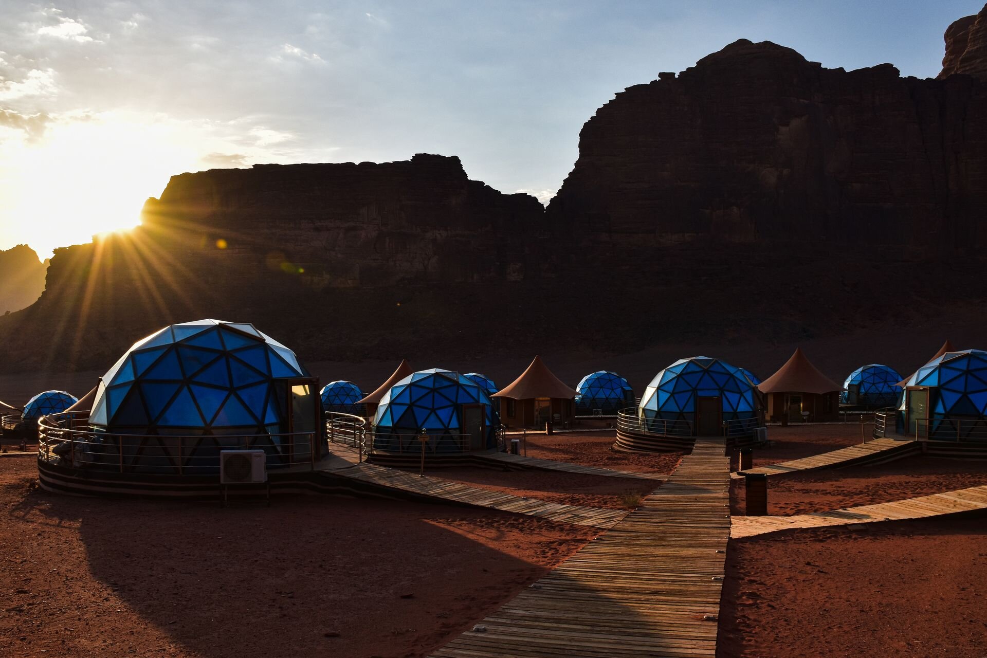 The sun rising behind the cliffs over the glass domes of a luxury camp in Wadi Rum, Jordan