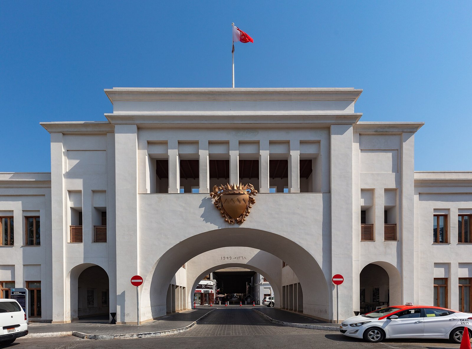 The white facade of Bab Al Bahrain, the historic gateway to the Manama souq, under a clear blue sky.