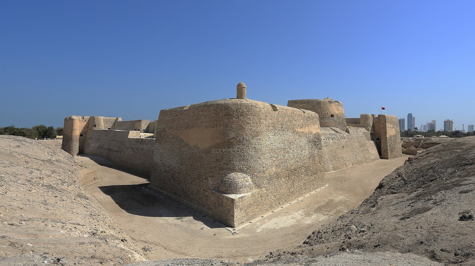 The ramparts of Qal'at al-Bahrain, the UNESCO-listed Bahrain Fort, under a clear blue sky.
