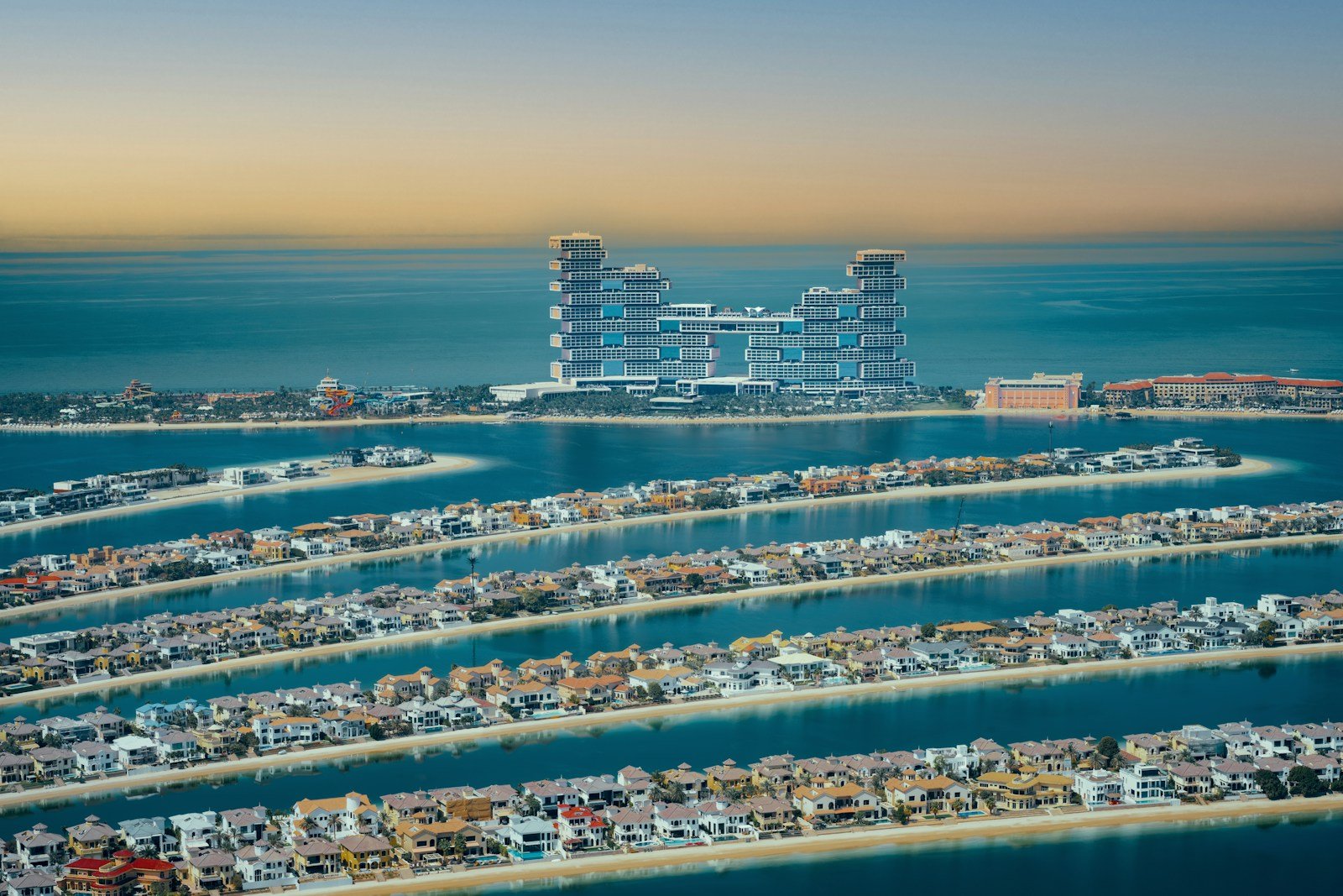 Atlantis The Royal rising at the crown of the Palm Jumeirah, its fronds lined with waterfront villas, at golden hour.