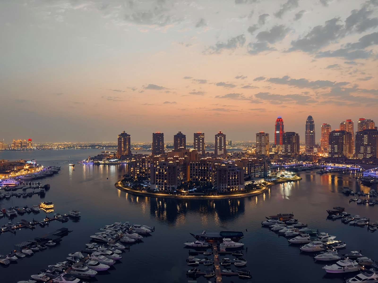 Yachts moored in the marinas of The Pearl-Qatar as the waterfront towers light up at dusk, Doha.