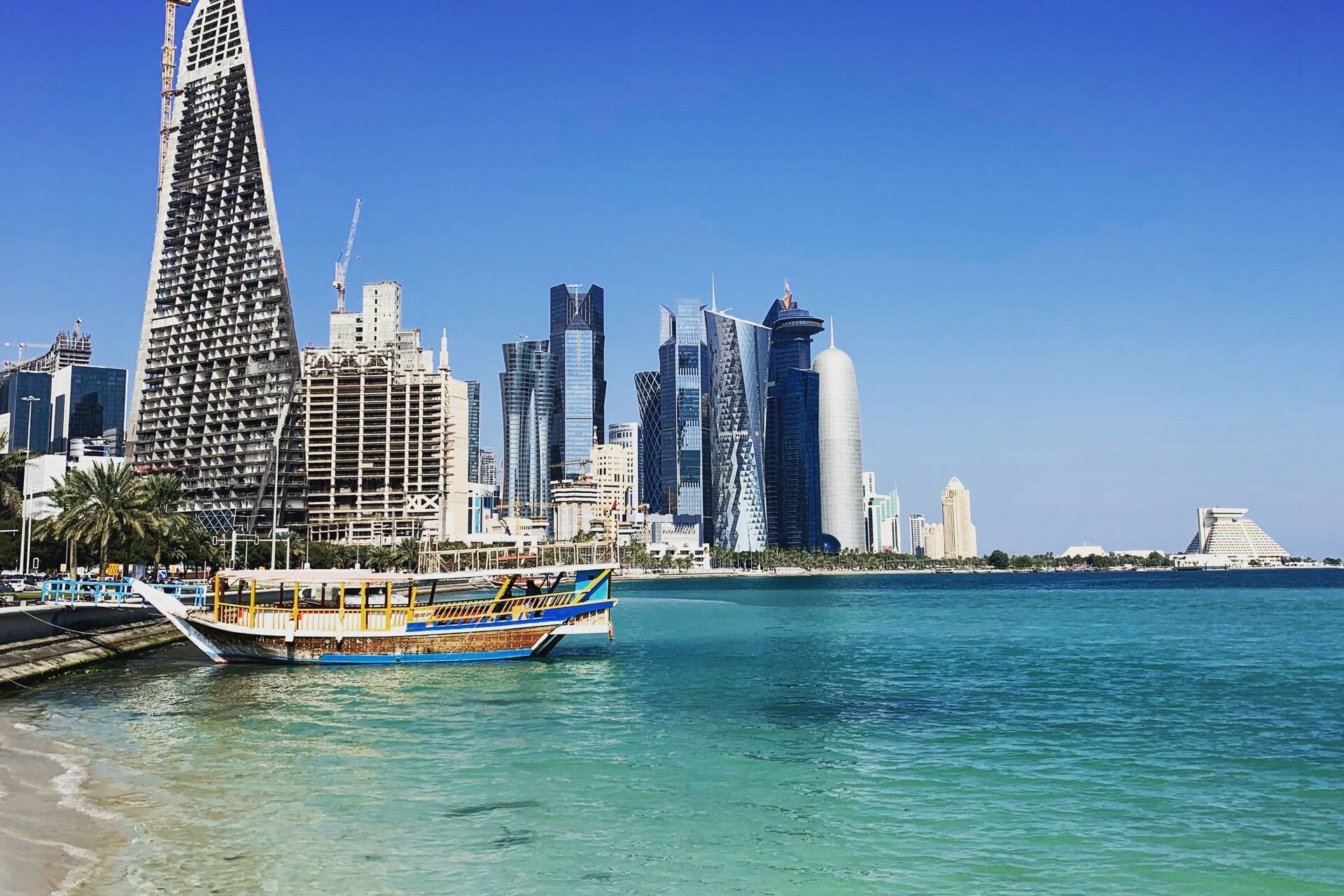 A dhow on the turquoise water of the Doha Corniche, with the towers of West Bay beyond