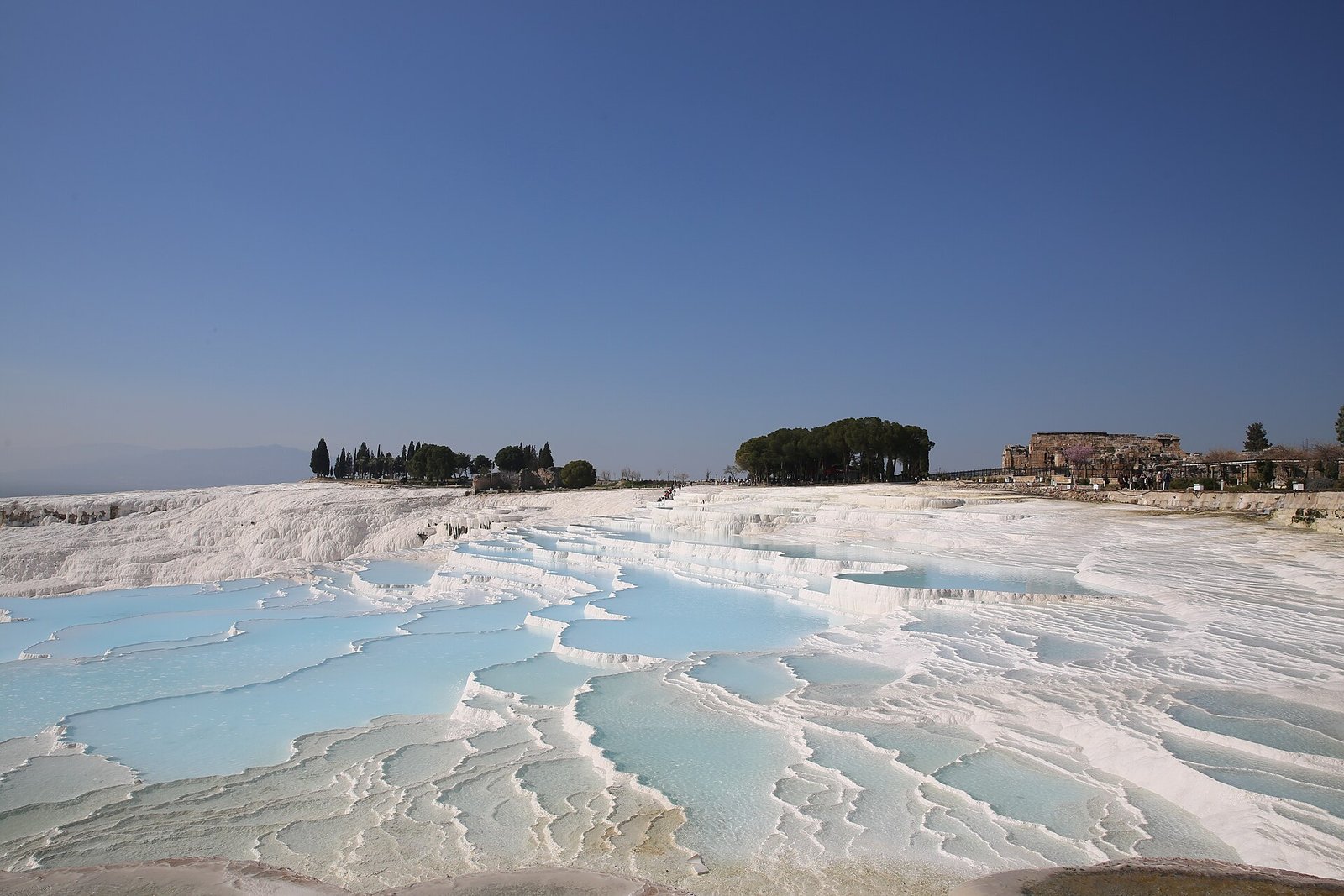 The white travertine terraces and turquoise pools of Pamukkale under a deep blue sky.