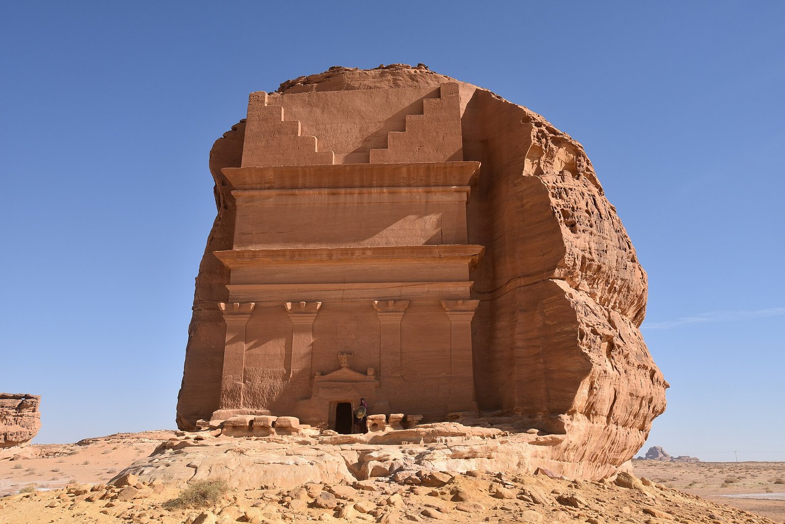 Qasr al-Farid, the lone Nabataean tomb carved into a sandstone boulder at Hegra, under a clear blue sky.
