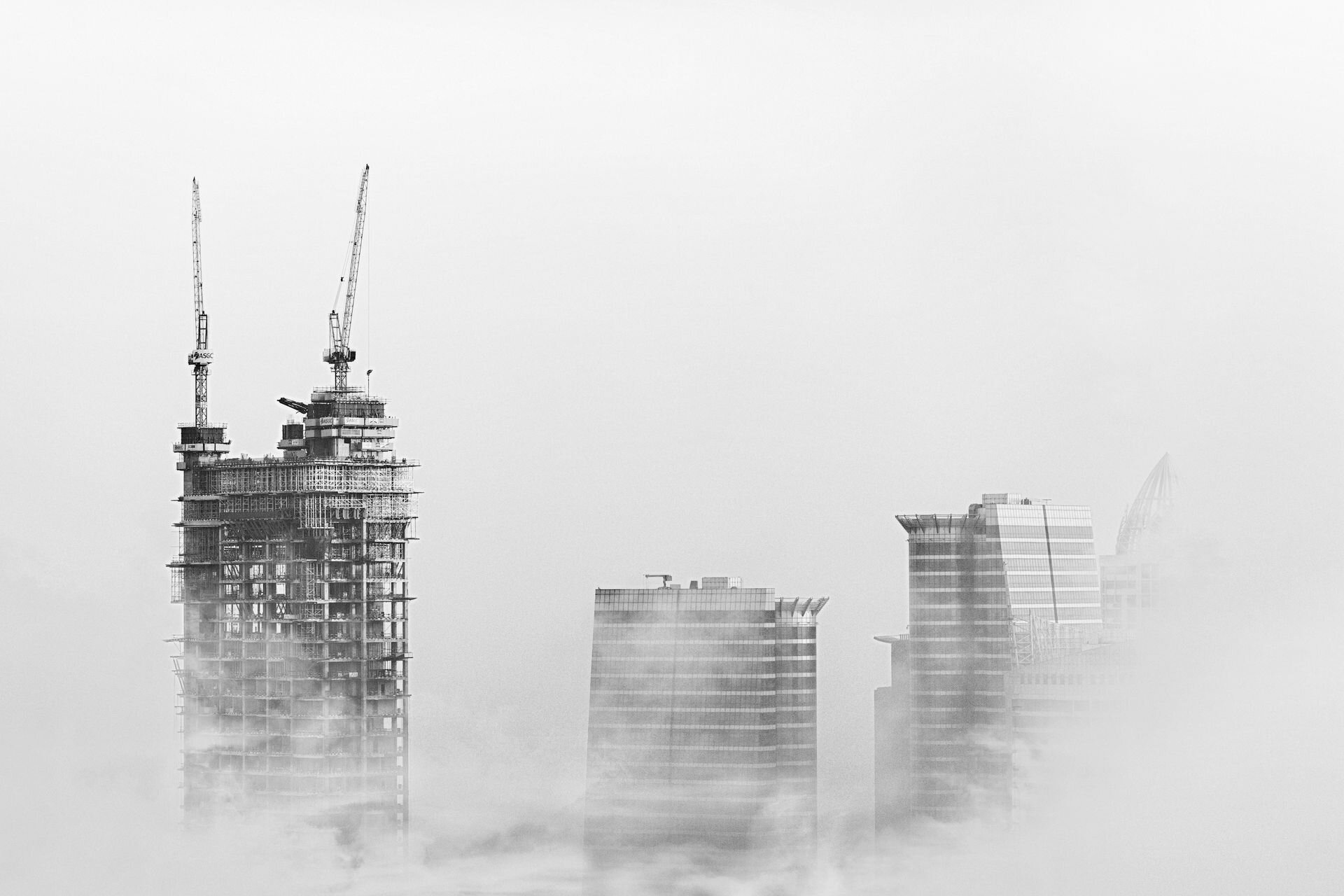 Tower cranes rising above morning fog over new towers in Dubai