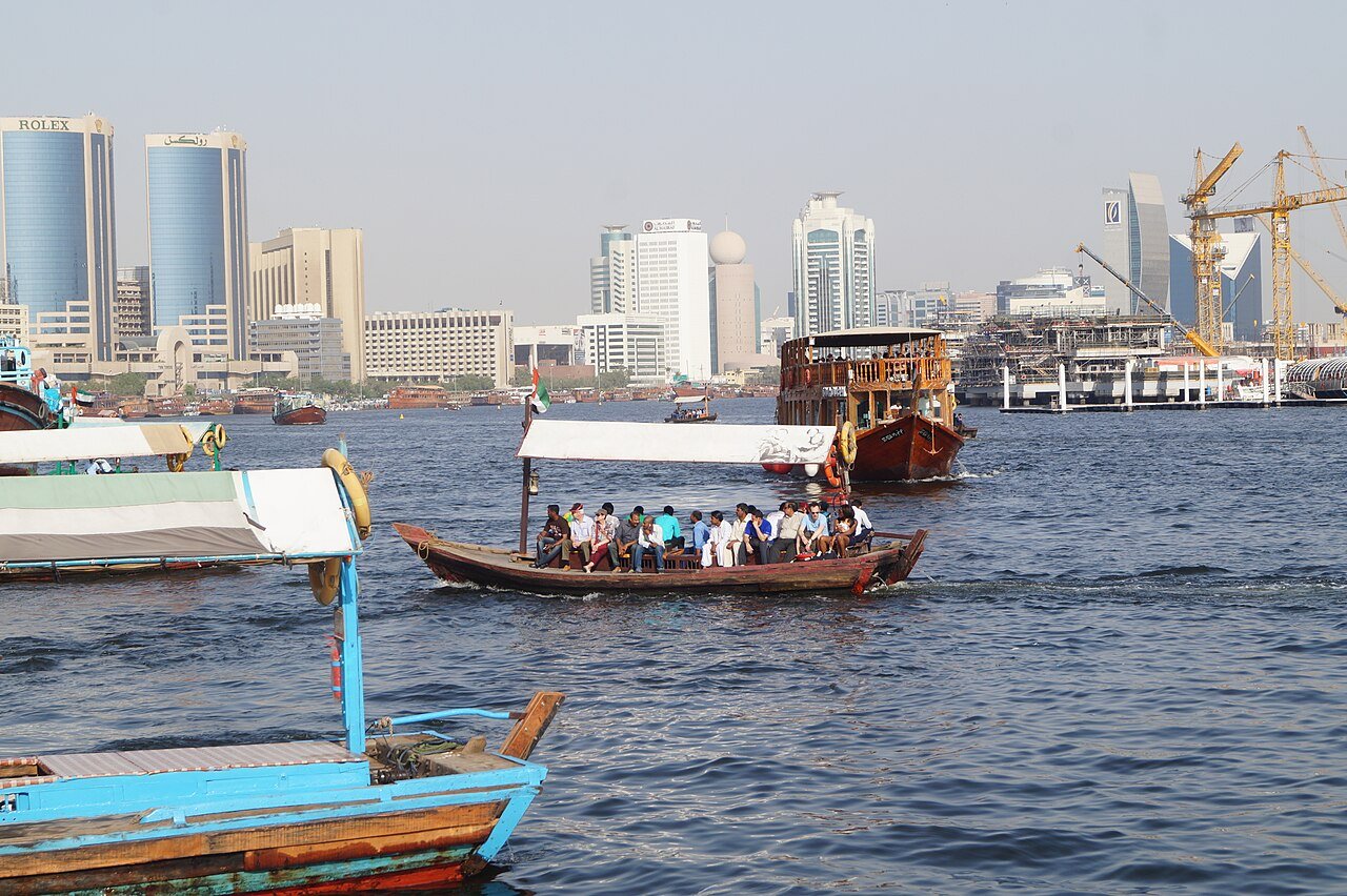 A wooden abra ferrying passengers across Dubai Creek, the towers of Deira beyond.