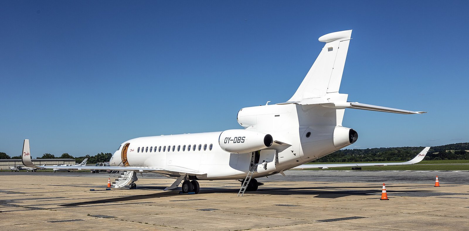 A white Dassault Falcon 8X business jet with its airstair lowered on the apron under a deep blue sky.