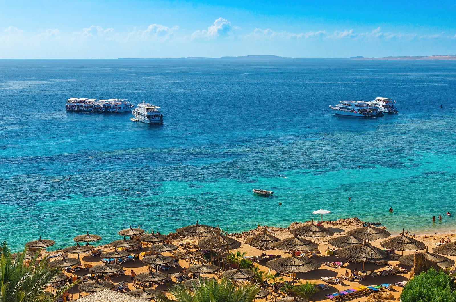 Thatched parasols on Gold Beach at Ras Um Sid, Sharm El Sheikh, above a turquoise Red Sea reef with dive boats