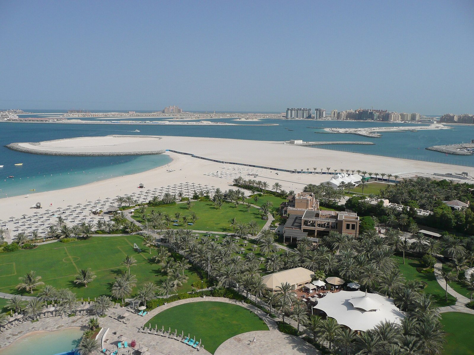 Resort gardens and a wide white beach in Dubai, with the Palm Jumeirah and Atlantis on the horizon